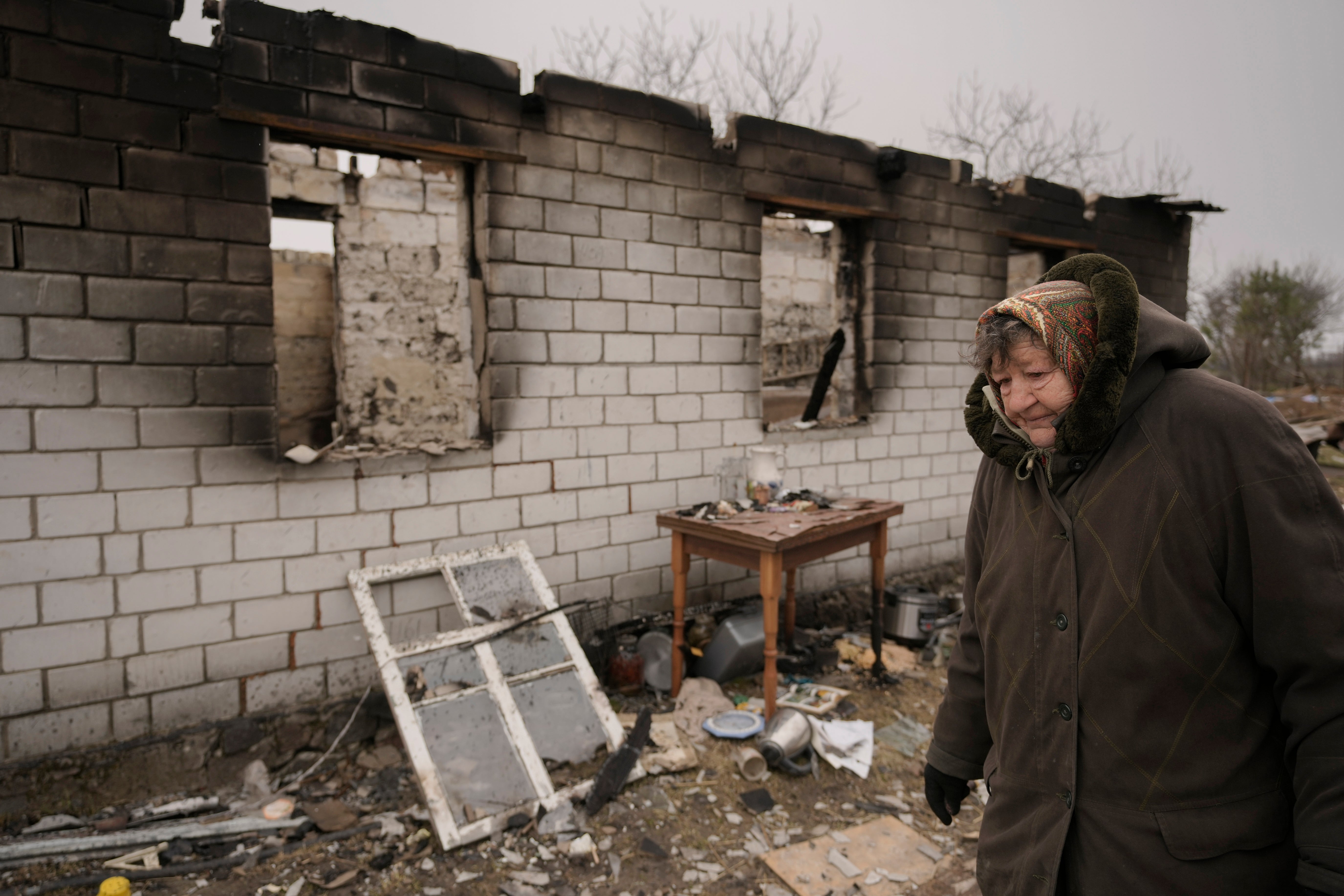 A woman walks by a house destroyed while her village was occupied by Russian troops in Andriivka