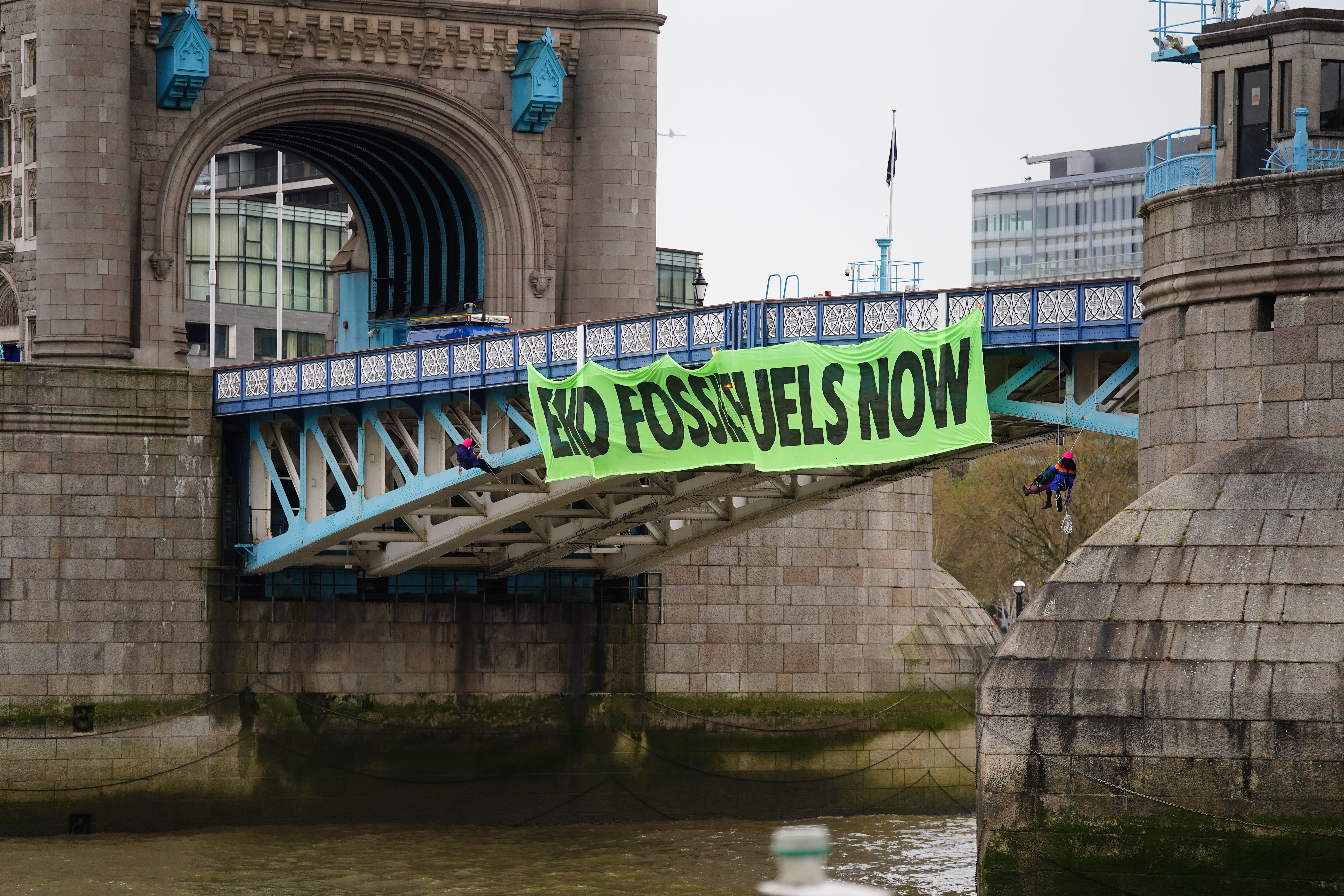 Activists from Extinction Rebellion hang from Tower Bridge on suspension cords beside a giant banner that reads ‘End fossil fuels now’ (Victoria Jones/PA)