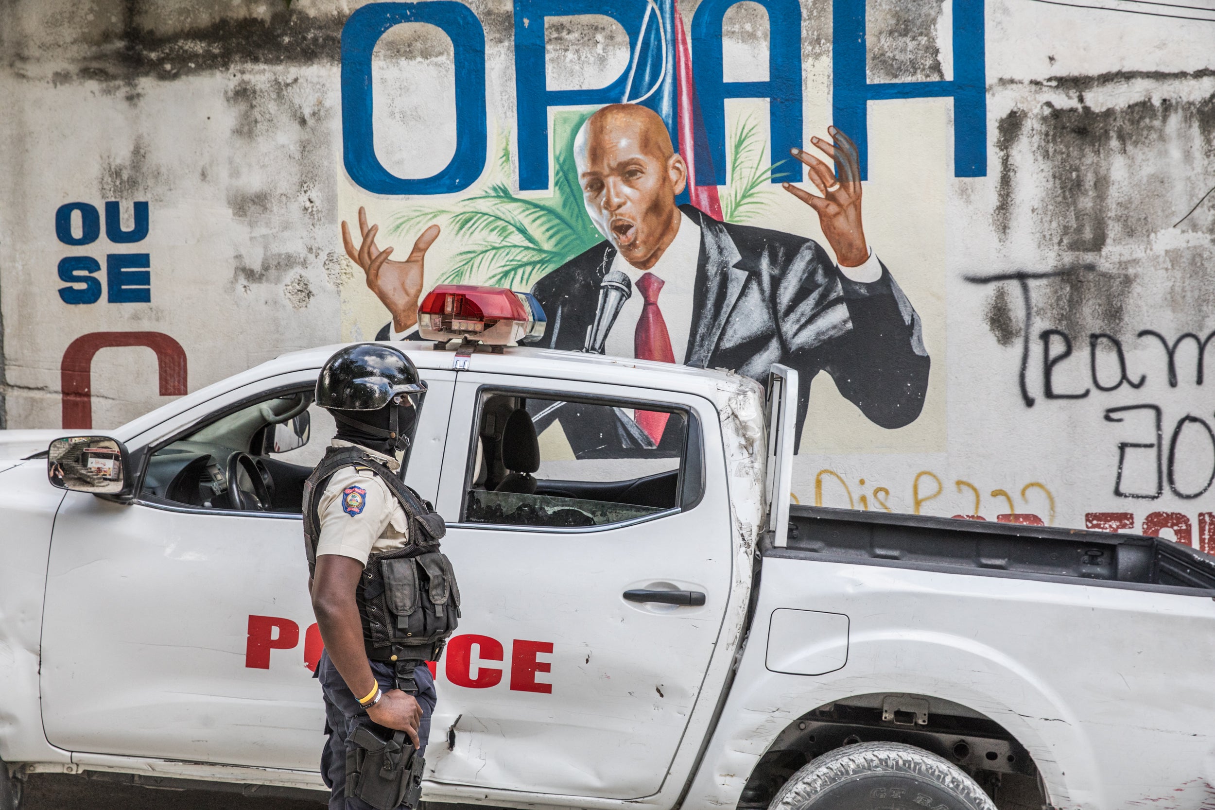 A police officer stands by a wall painted with a mural of Moise