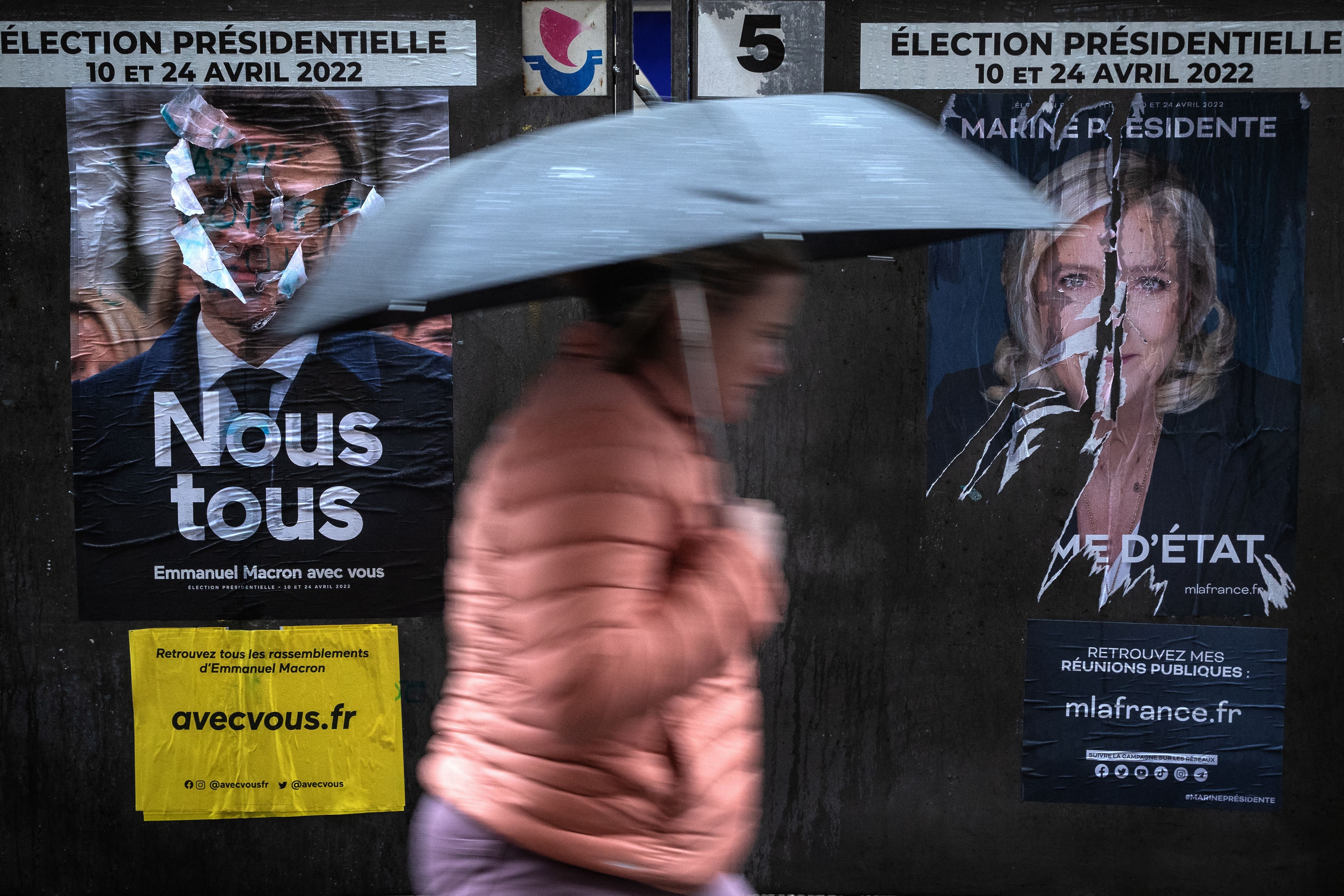 A pedestrian walks past torn campaign posters for Macron and Len Pen in Paris