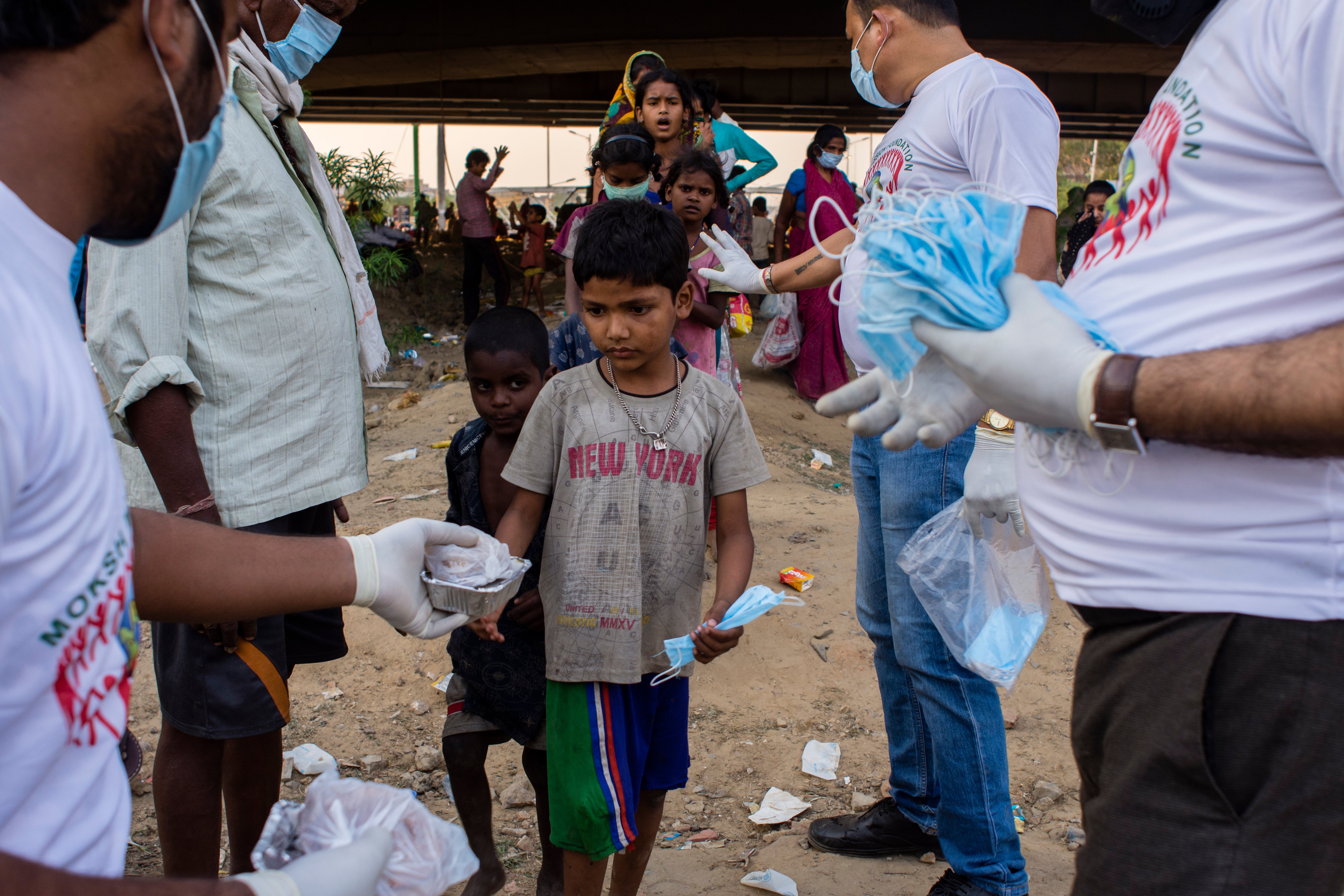 Children of Indian migrant workers receive free food and face masks as they wait to cross the border from Delhi