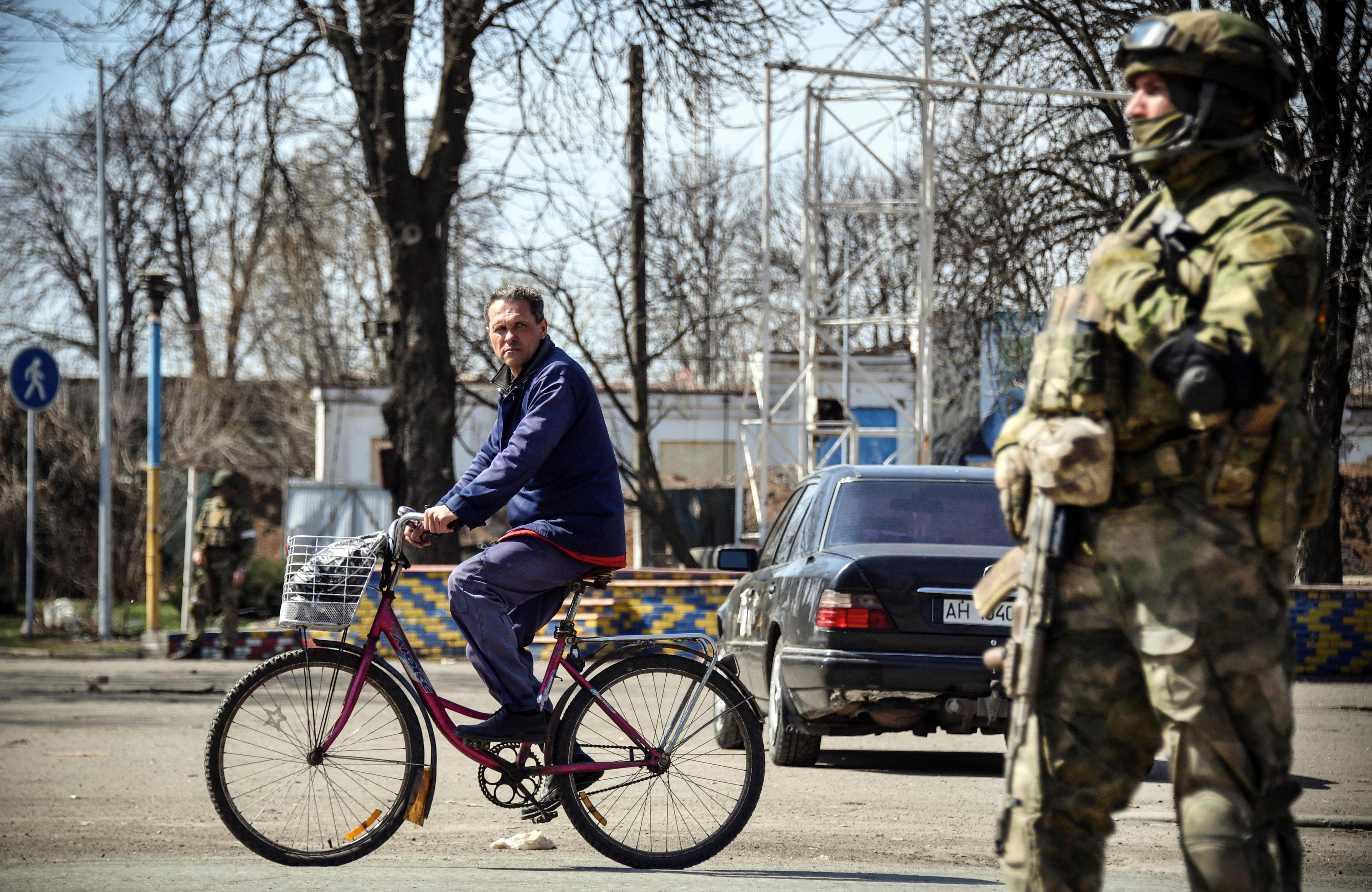 A man rides a bicycle by a Russian soldier standing guard in Volnovakhaa in the self-proclaimed Donetsk People's Republic