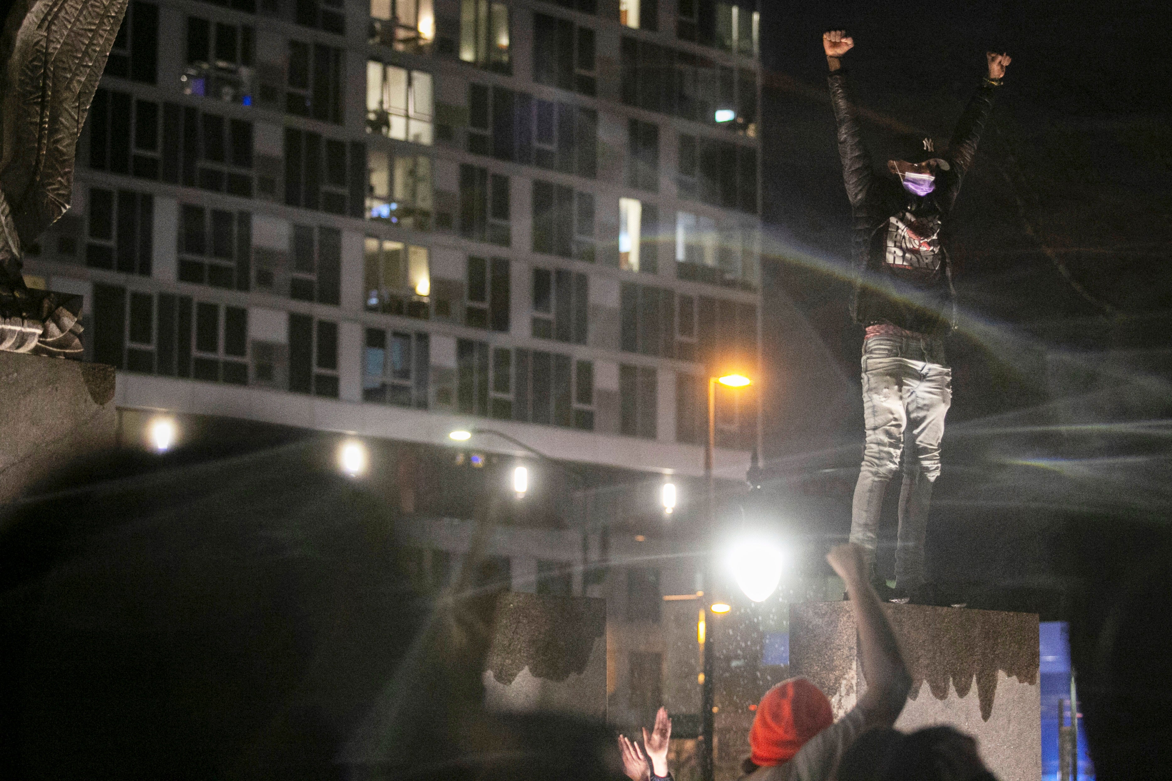 A protester stands on top of a statue as others march into Veterans Memorial Park from the Grand Rapids Police Department