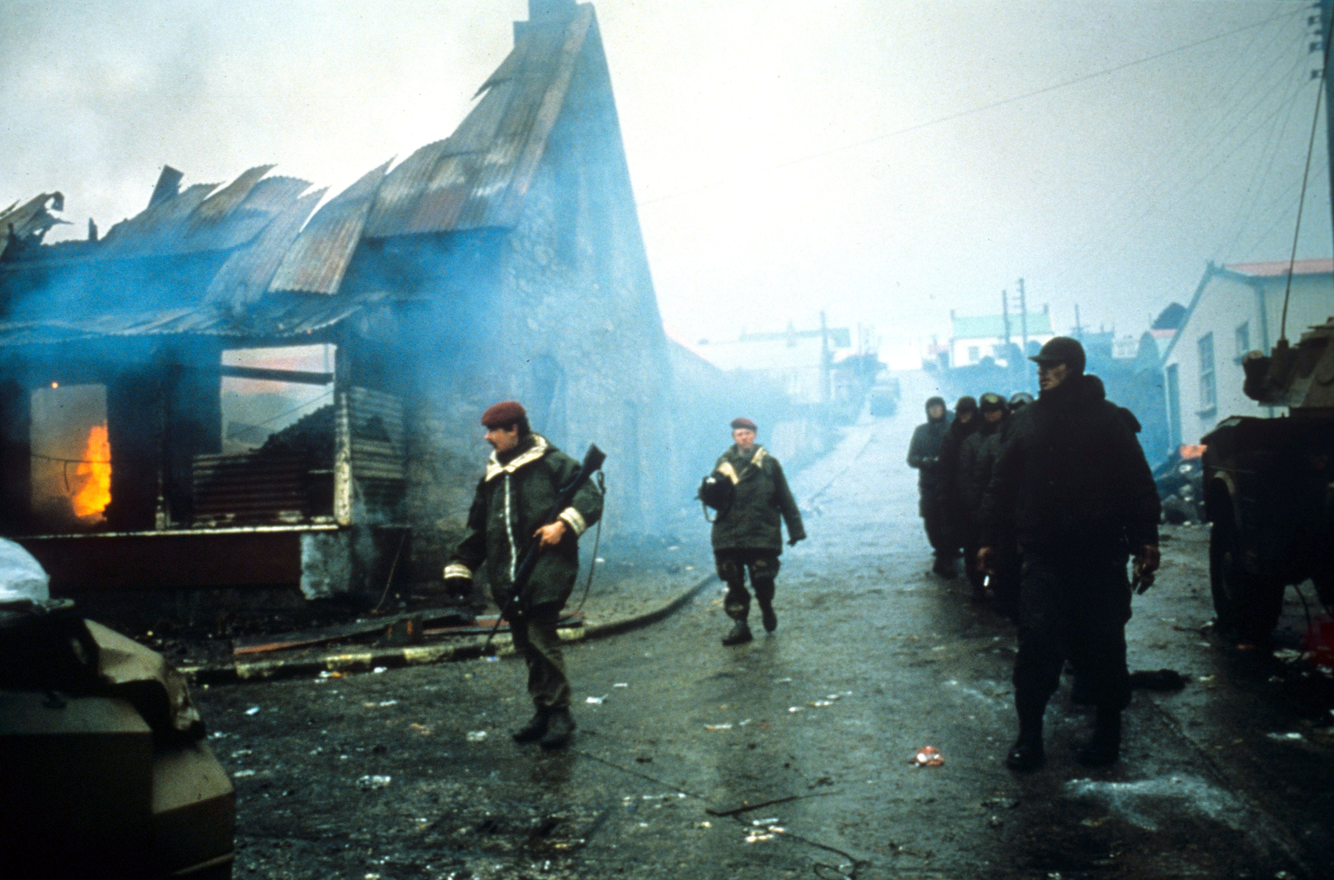 A line of Argentine prisoners of war are marched past a still-burning building in Port Stanley during a house-to-house round-up in the final days of the conflict