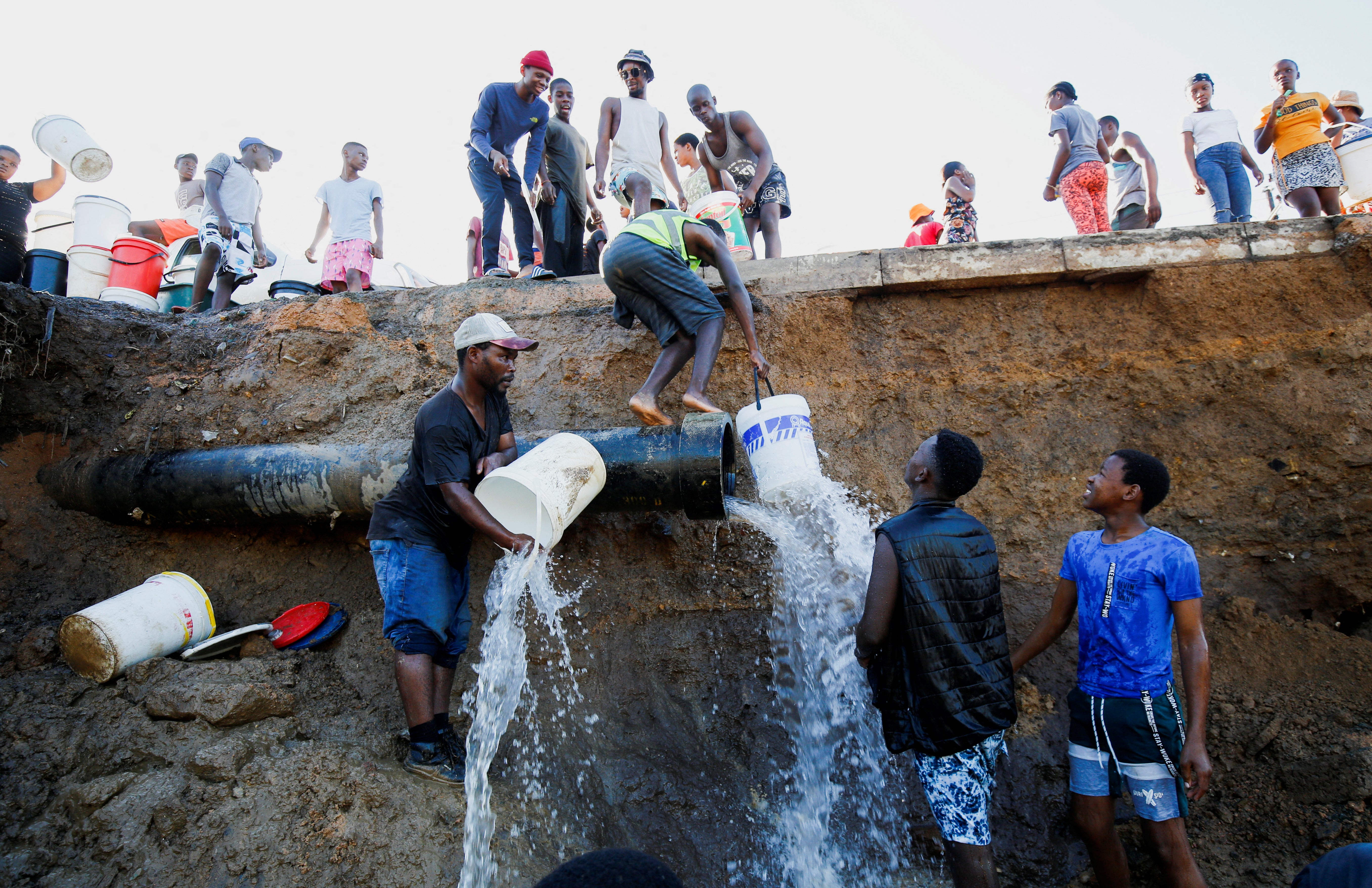 People fill buckets from a broken water main after services were damaged by flooding