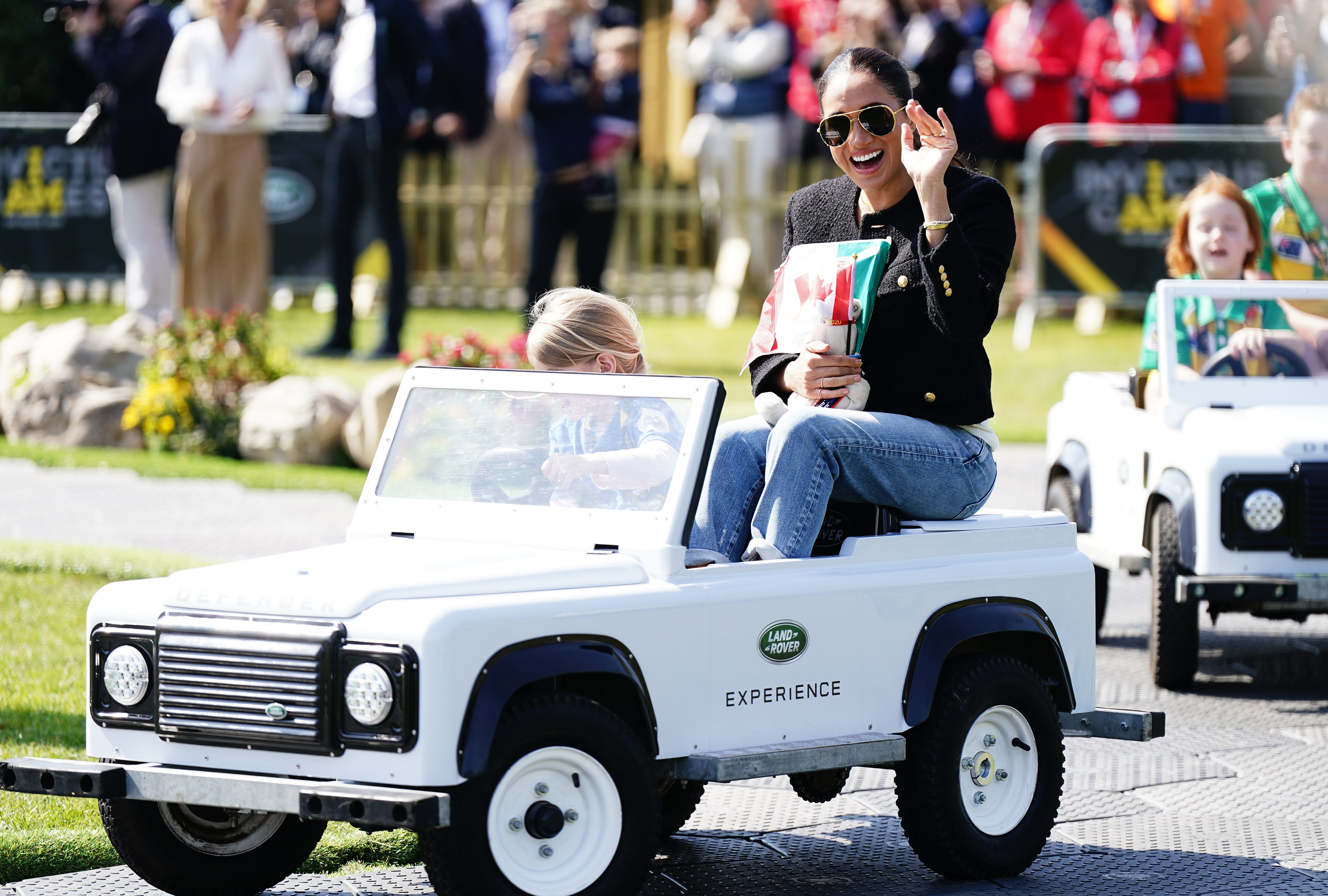 The Duchess of Sussex is driven by a child in a toy Land Rover at the Jaguar Land Rover Driving Challenge during the Invictus Games (PA)