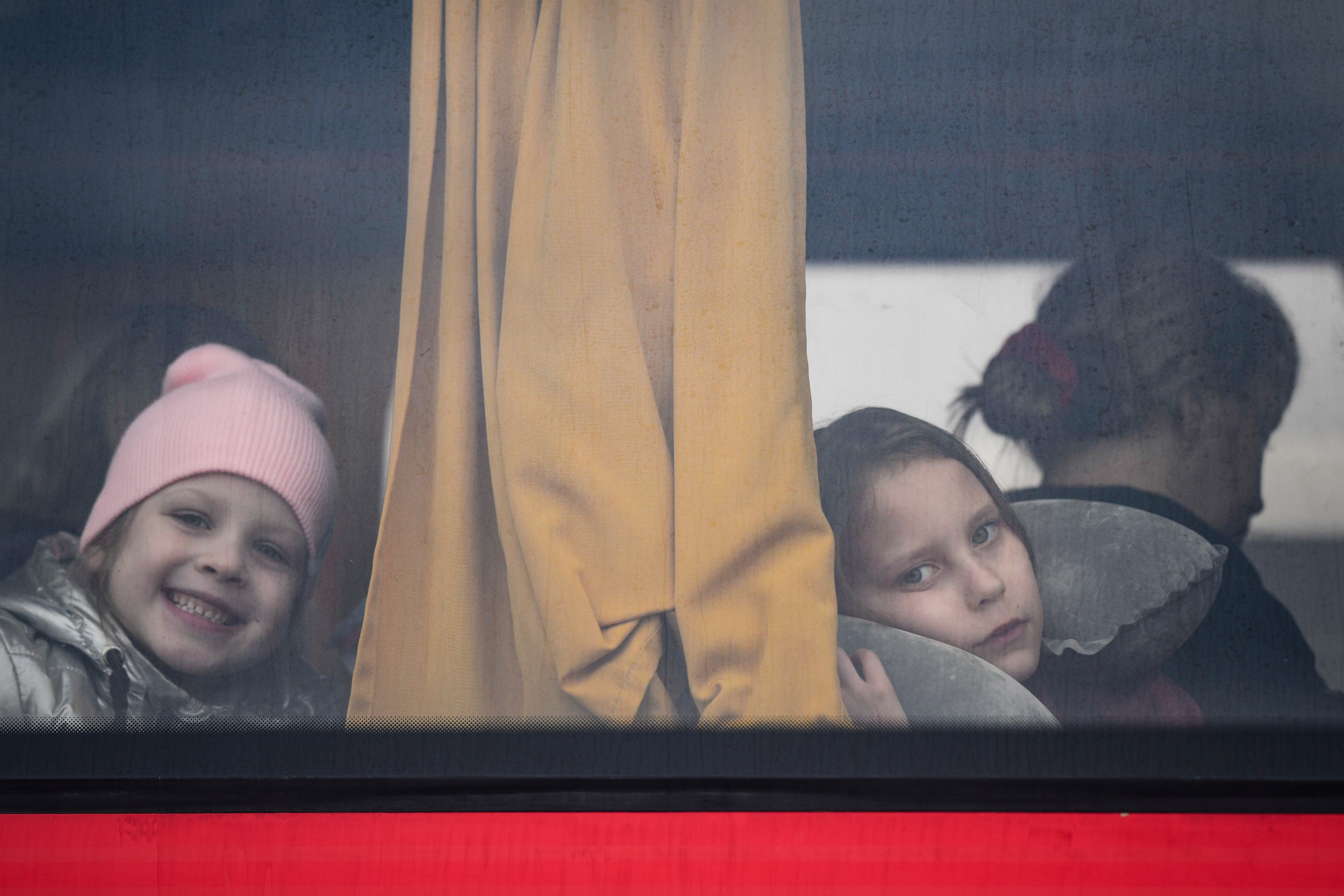 Children fleeing the war from Ukraine with their families look out the window of a bus after crossing the border into Poland