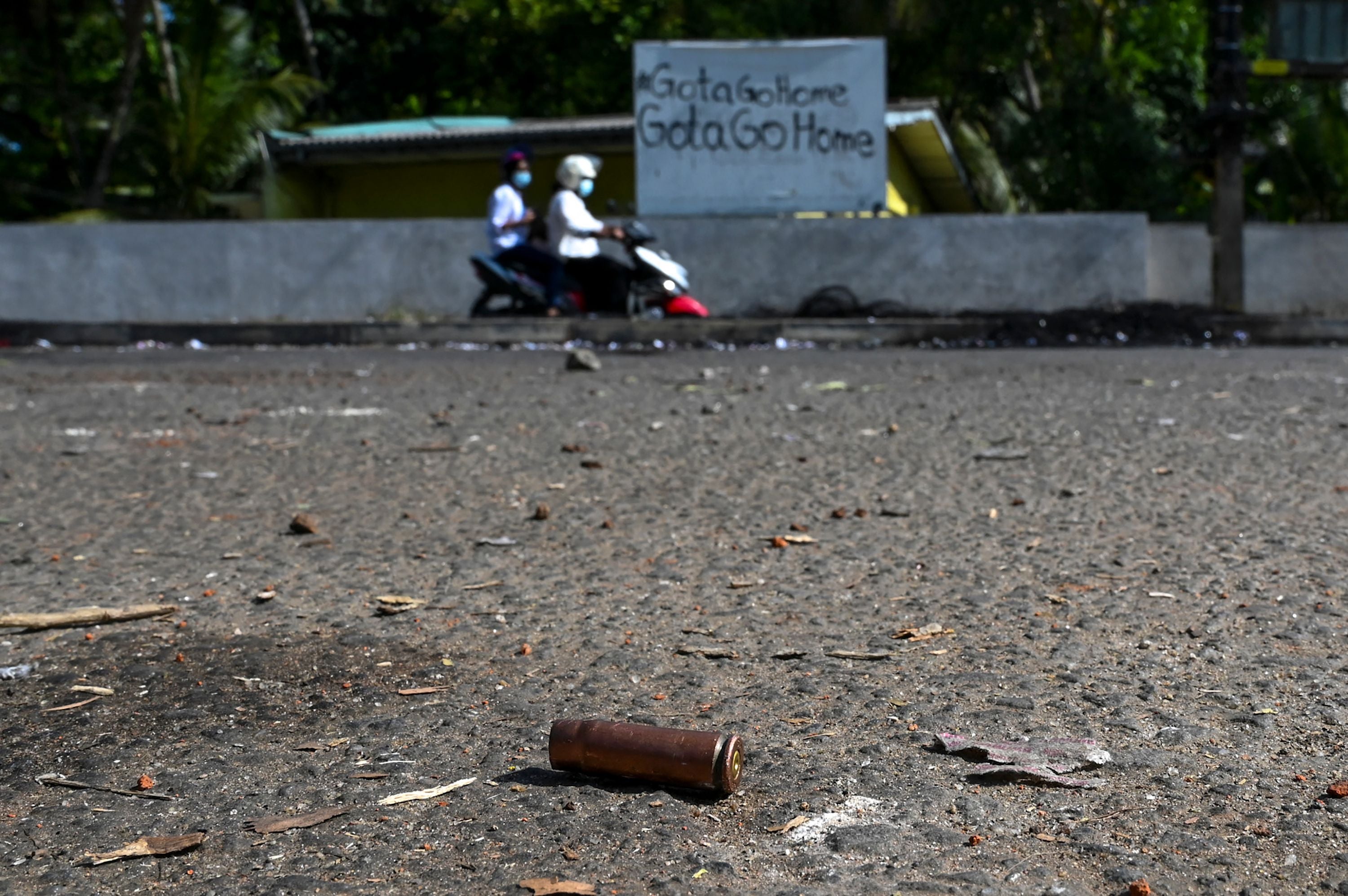 Motorists ride along a street past a spent cartridge in Rambukkana on 20 April, a day after police killed an anti-government demonstrator while dispersing a protest against the high fuel prices