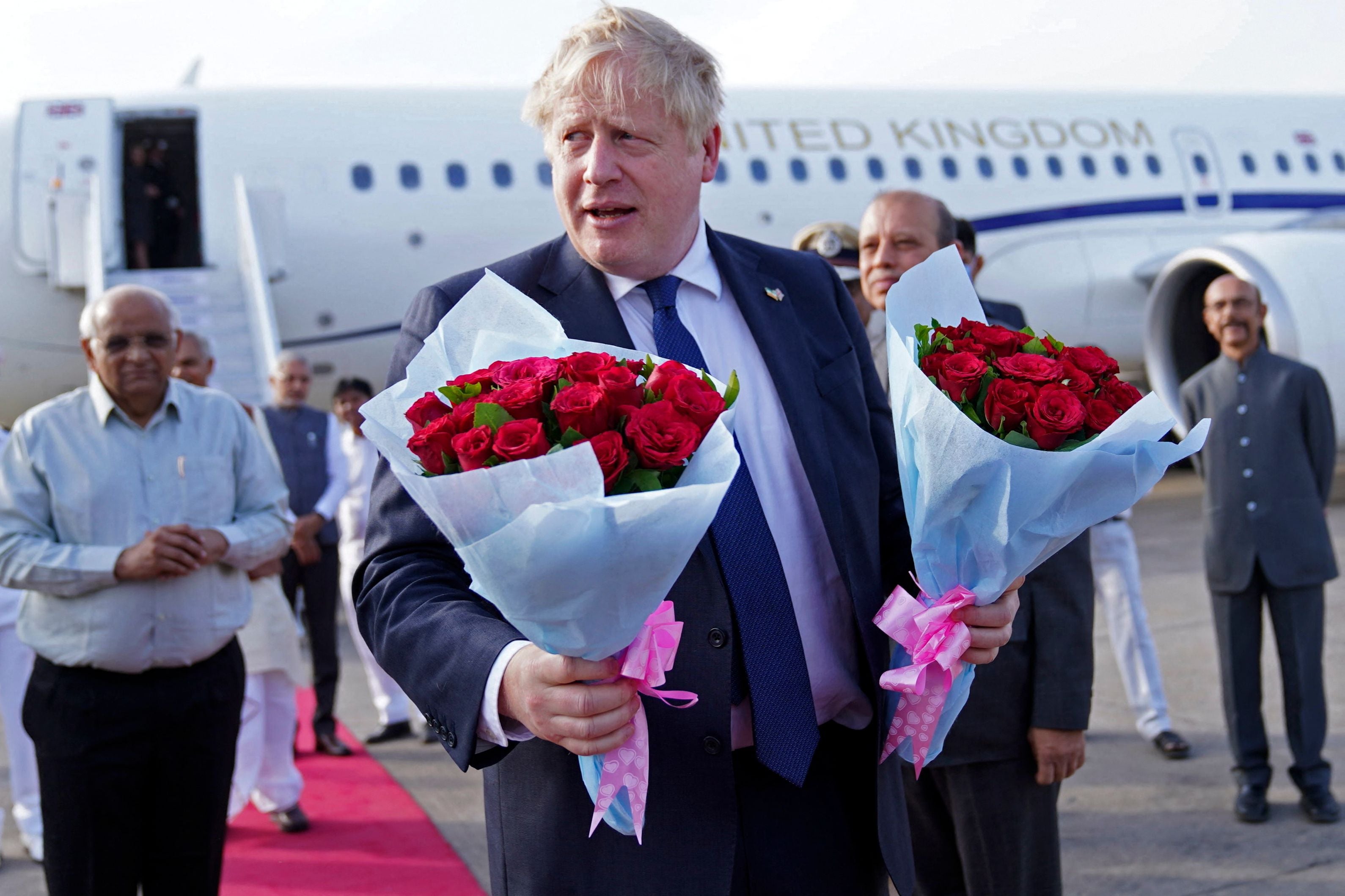 Boris Johnson holds flower bouquets after he was greeted by officials upon his arrival at the airport in Ahmedabad