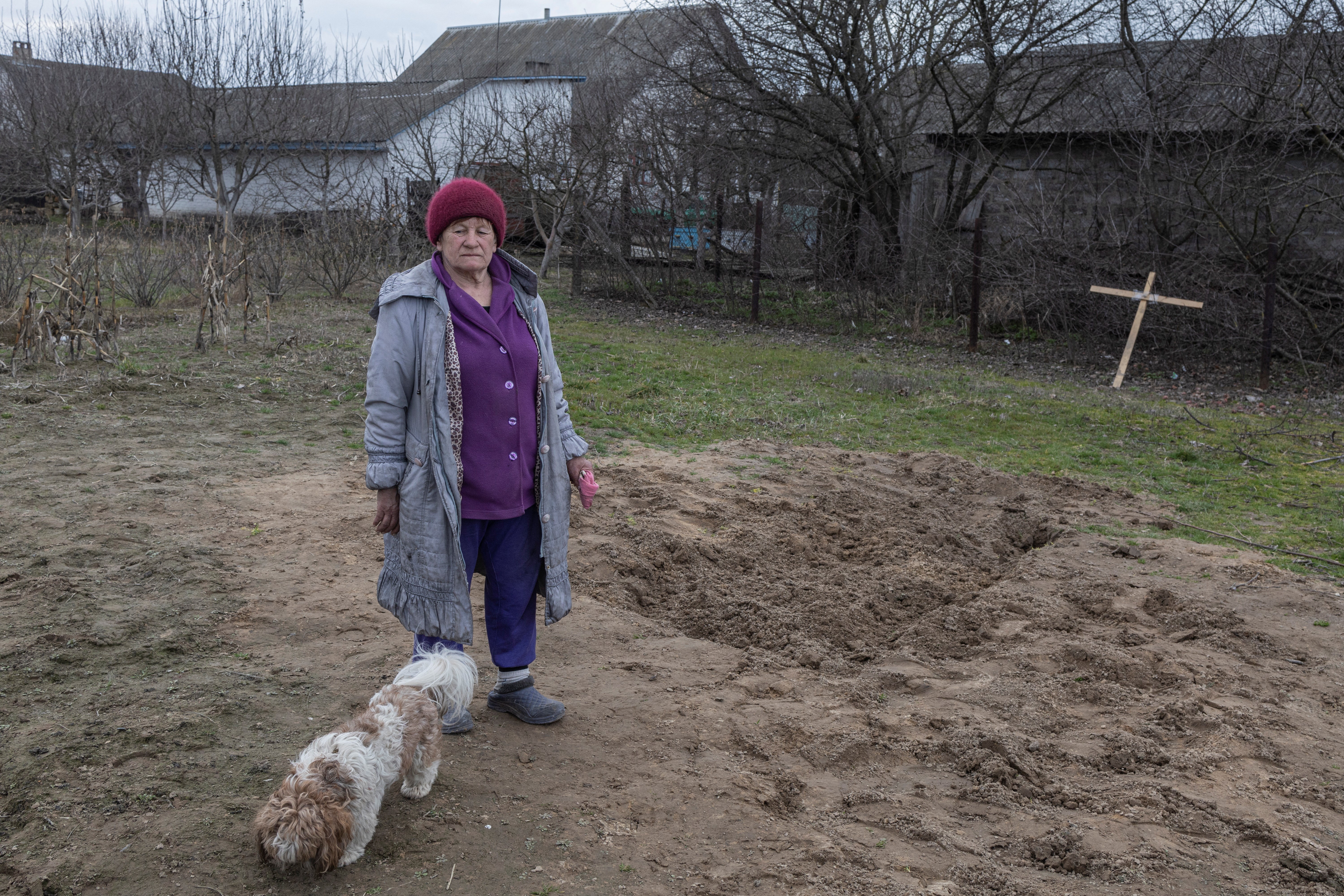 Tamara Klymchuk, 64, and her dog stand next to the grave of a local man