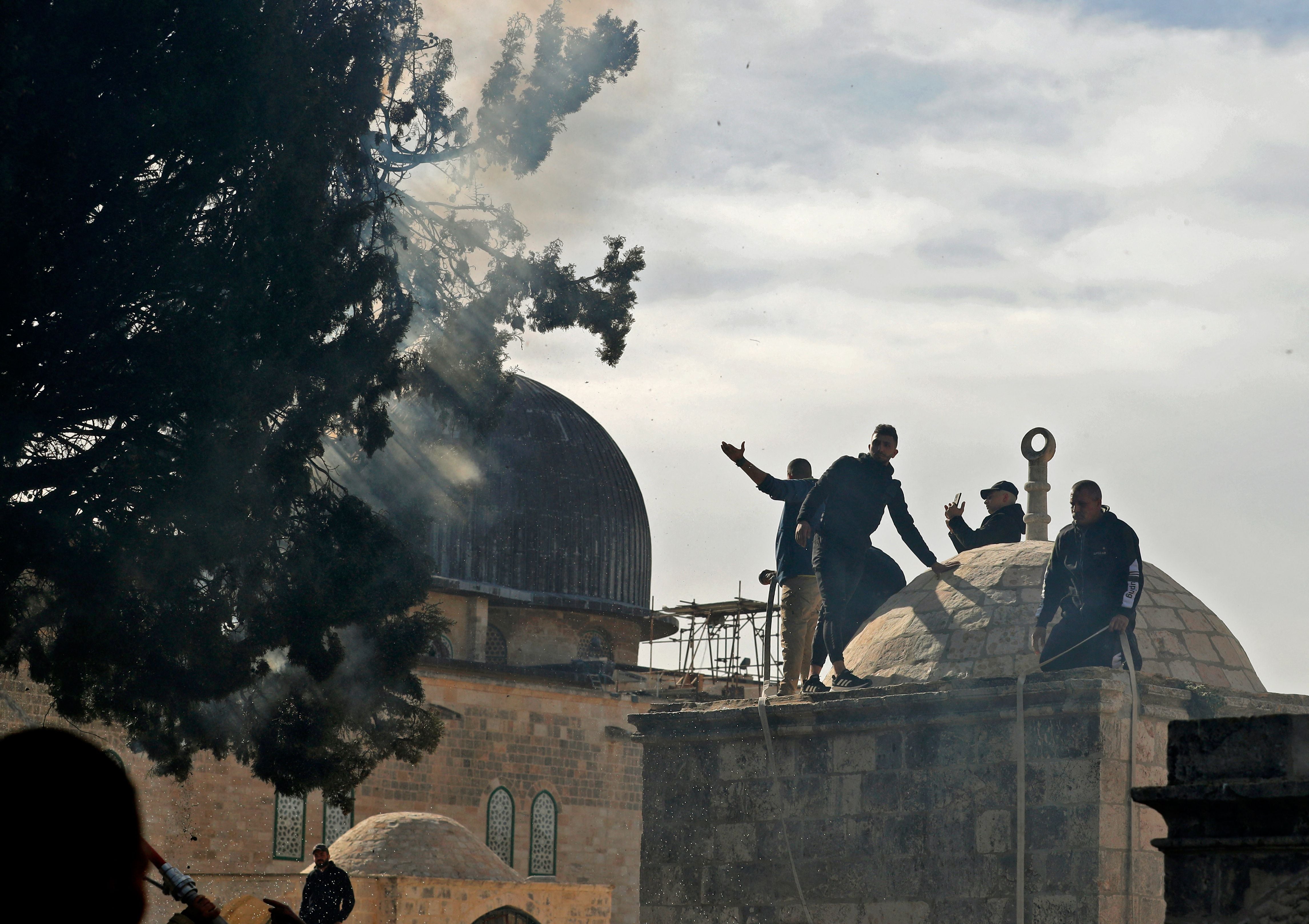 Palestinian men help firefighters douse flames which erupted in trees inside the Al-Aqsa Mosque complex