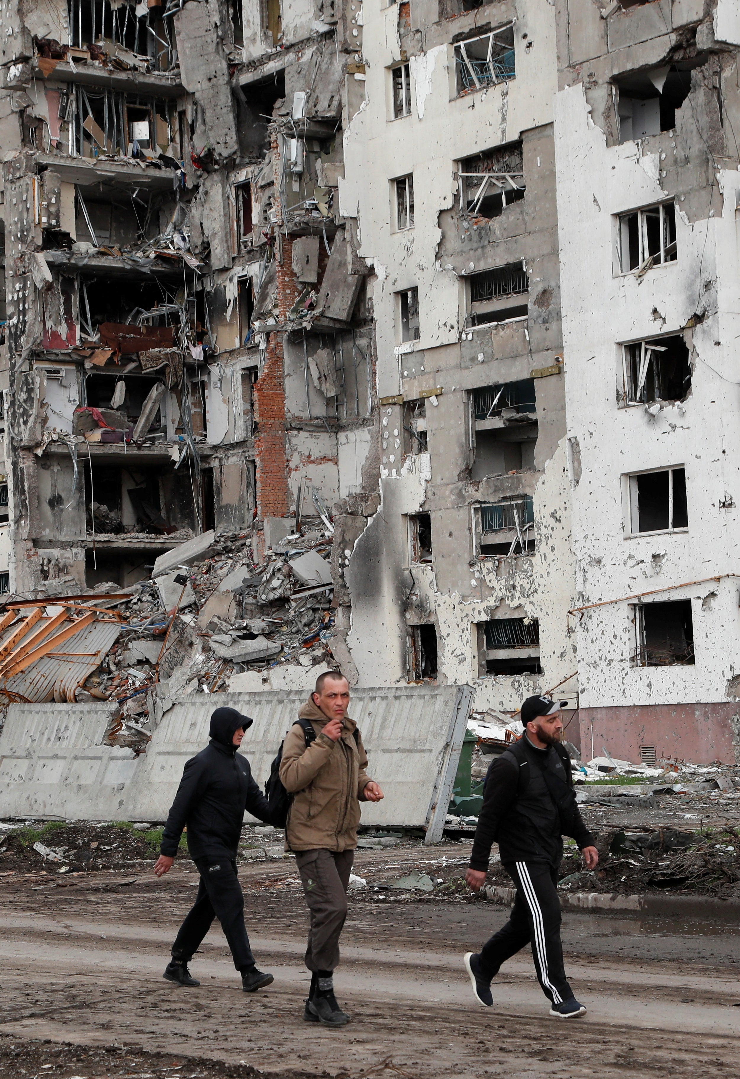 People walk along a street near a destroyed residential building in Mariupol