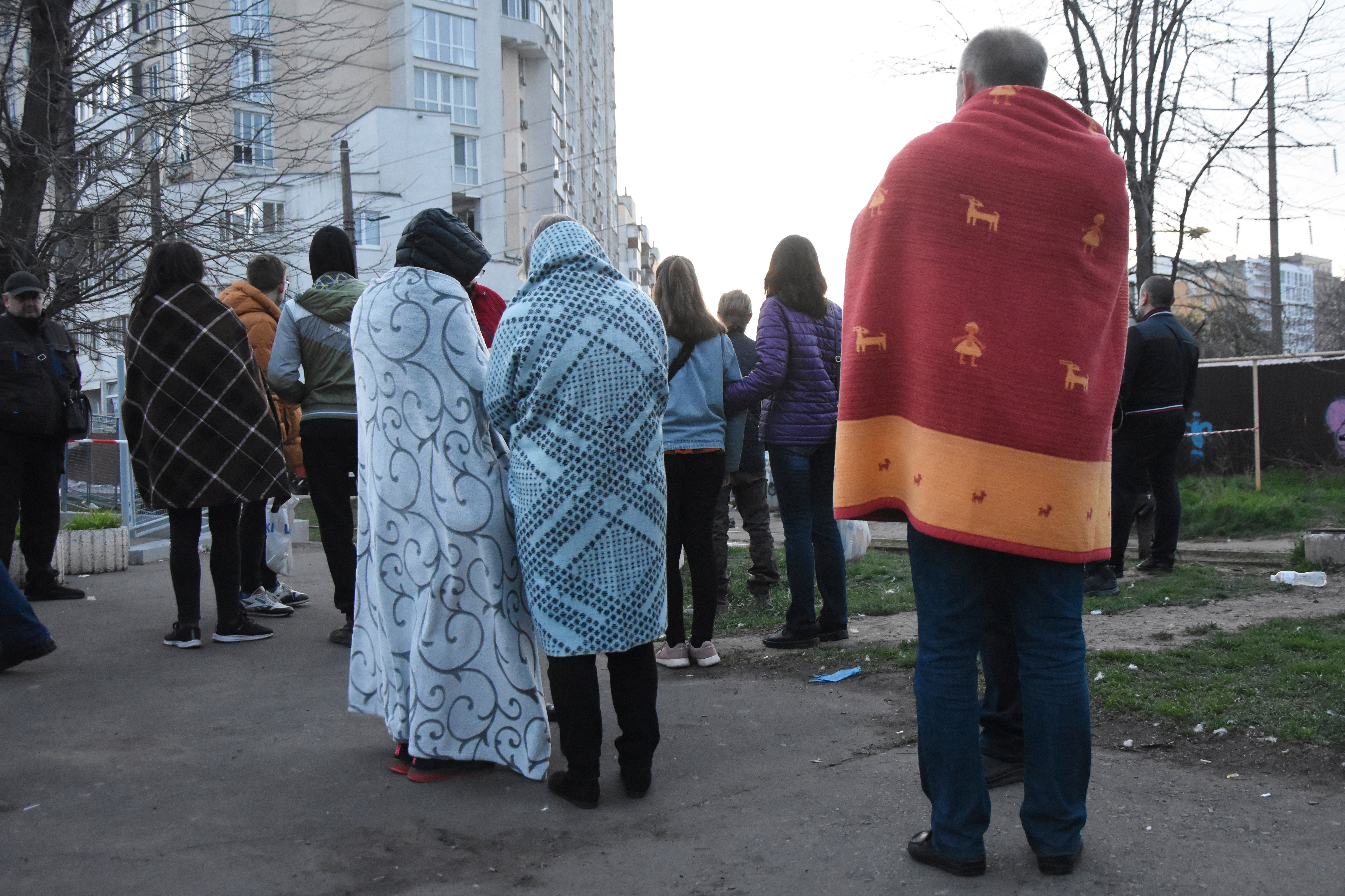 Residents stand covered by blankets next to their houses damaged by Russian shelling in Odesa