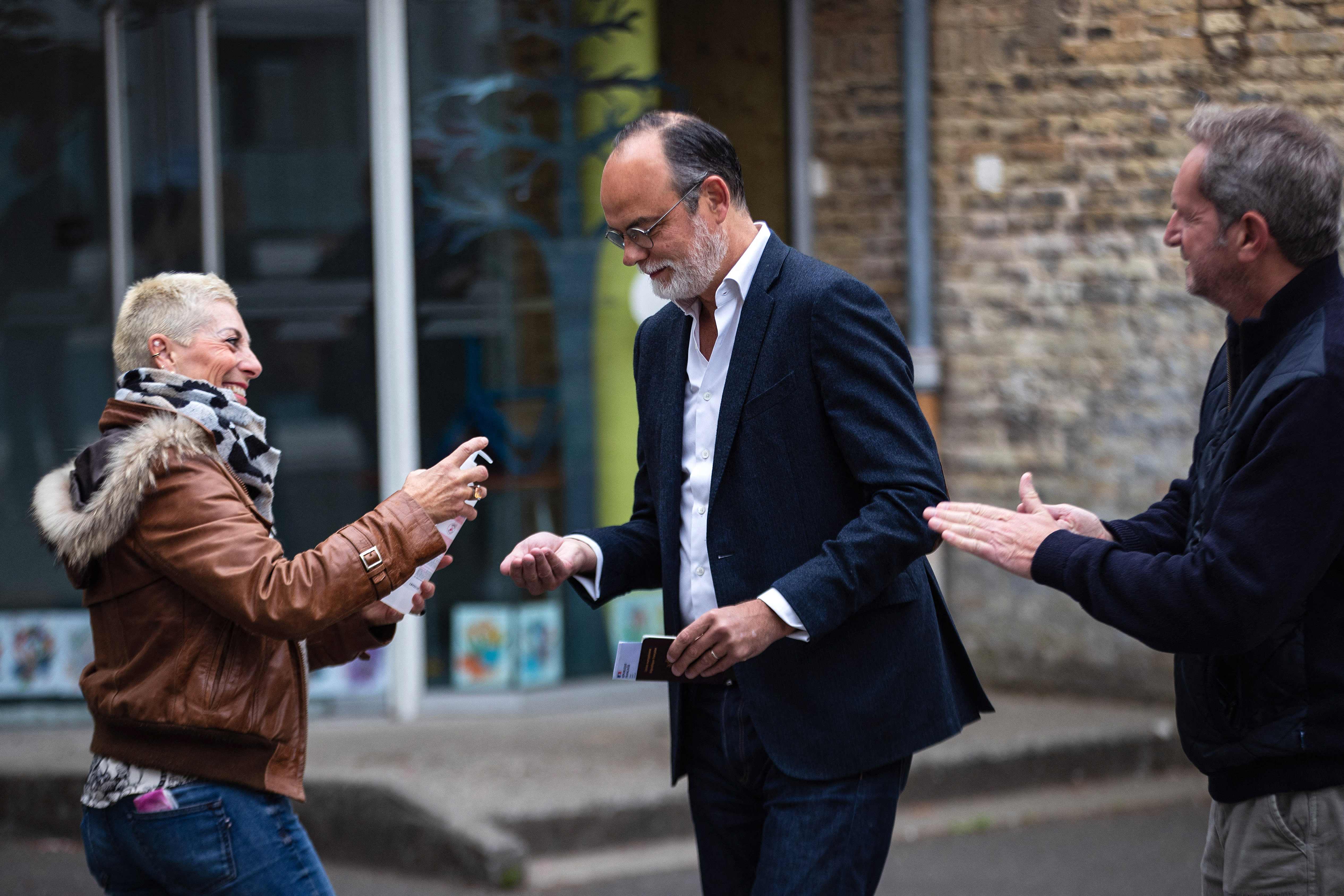 Former French Prime Minister Edouard Philippe (C) disinfects his hands as he queues to vote