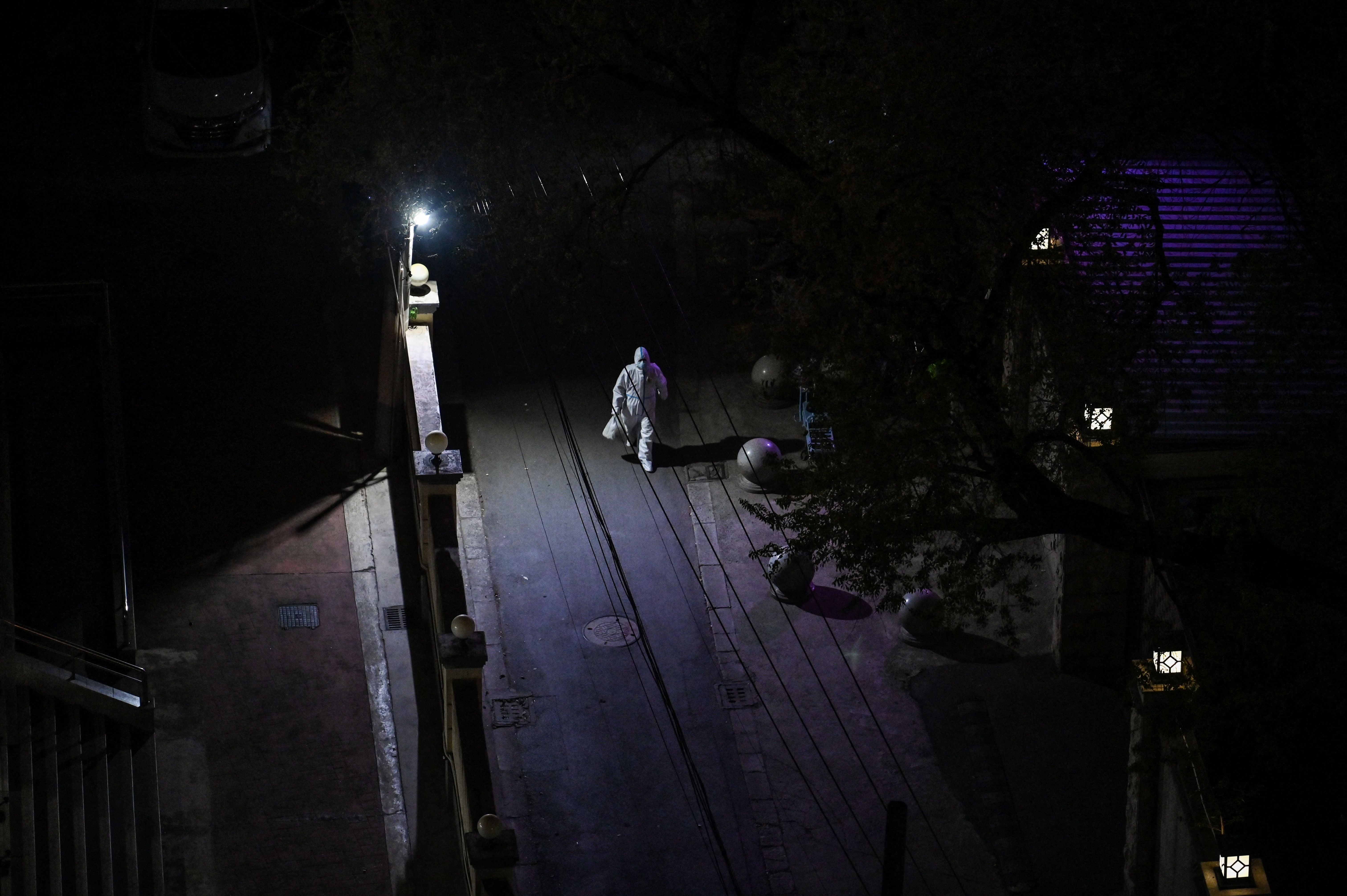 A worker wearing personal protective equipment (PPE) walks on a street at night during lockdown in the Jing’an district in Shanghai on April 10, 2022