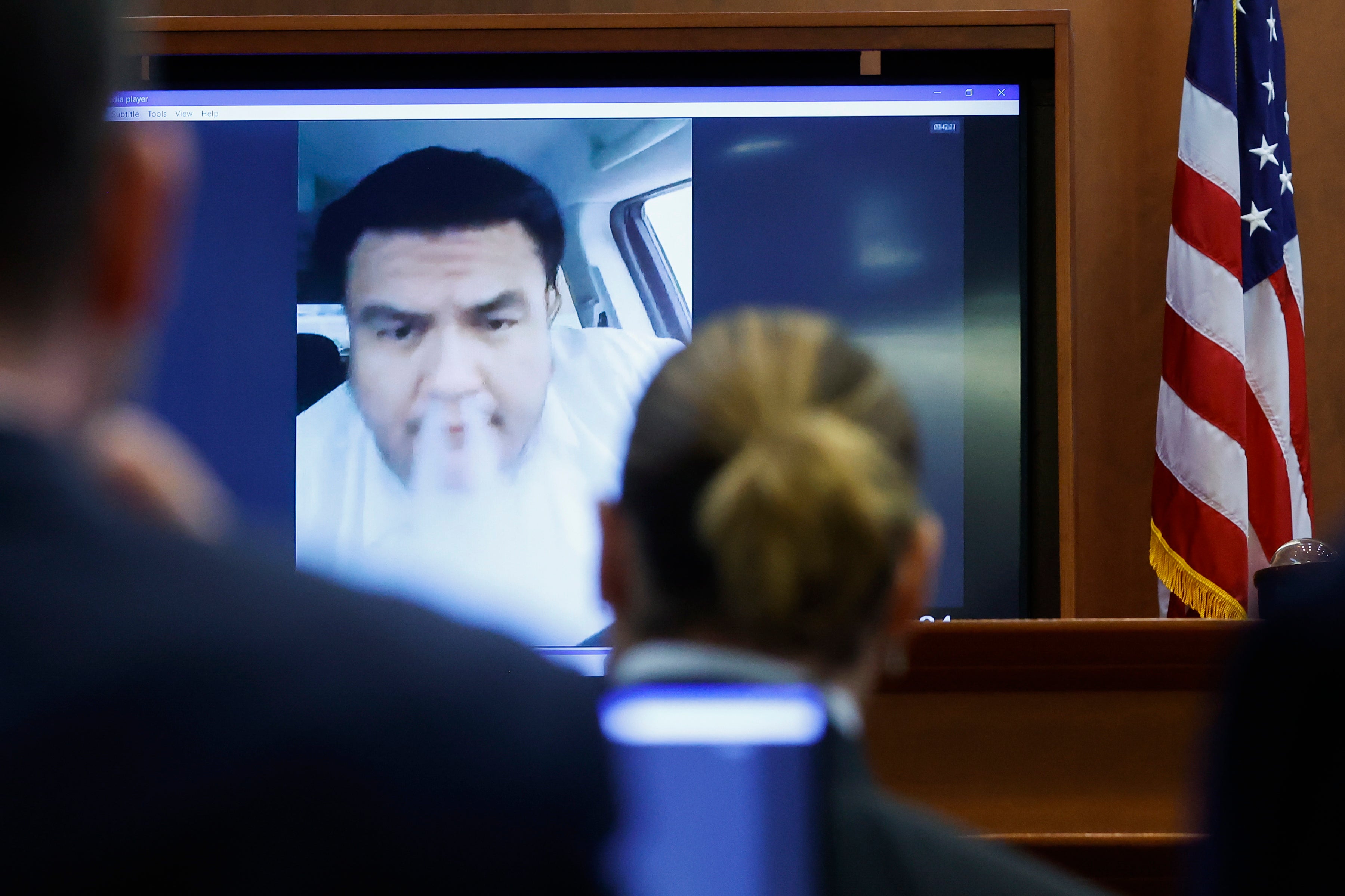 Johnny Depp watches a pre-recorded deposition testimony of Alejandro Romero, who appears on a screen blowing vape smoke out of his nose during the Depp v Heard defamation trial