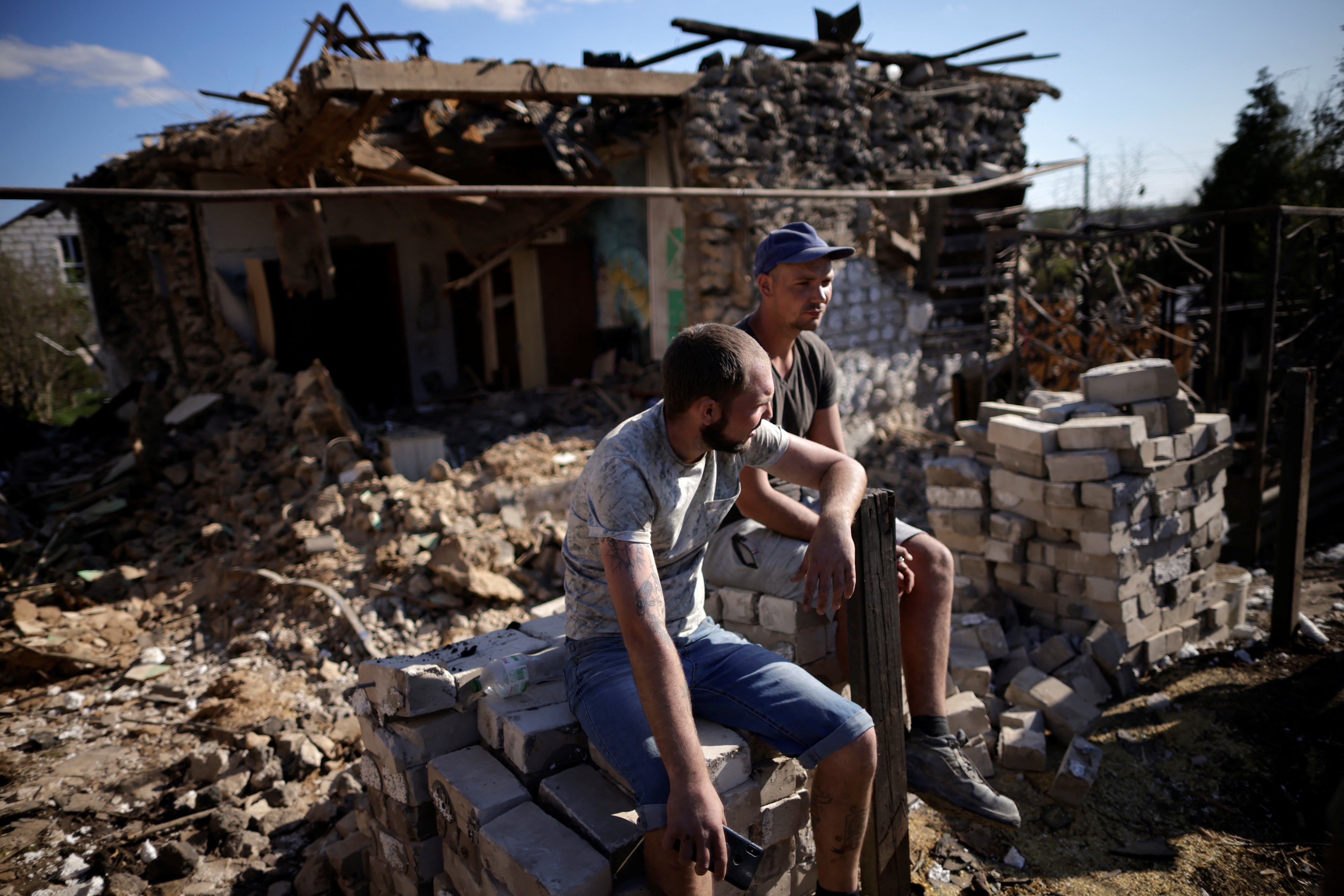 Men sit outside a house in Zaporizhzhia that was damaged by a missile attack