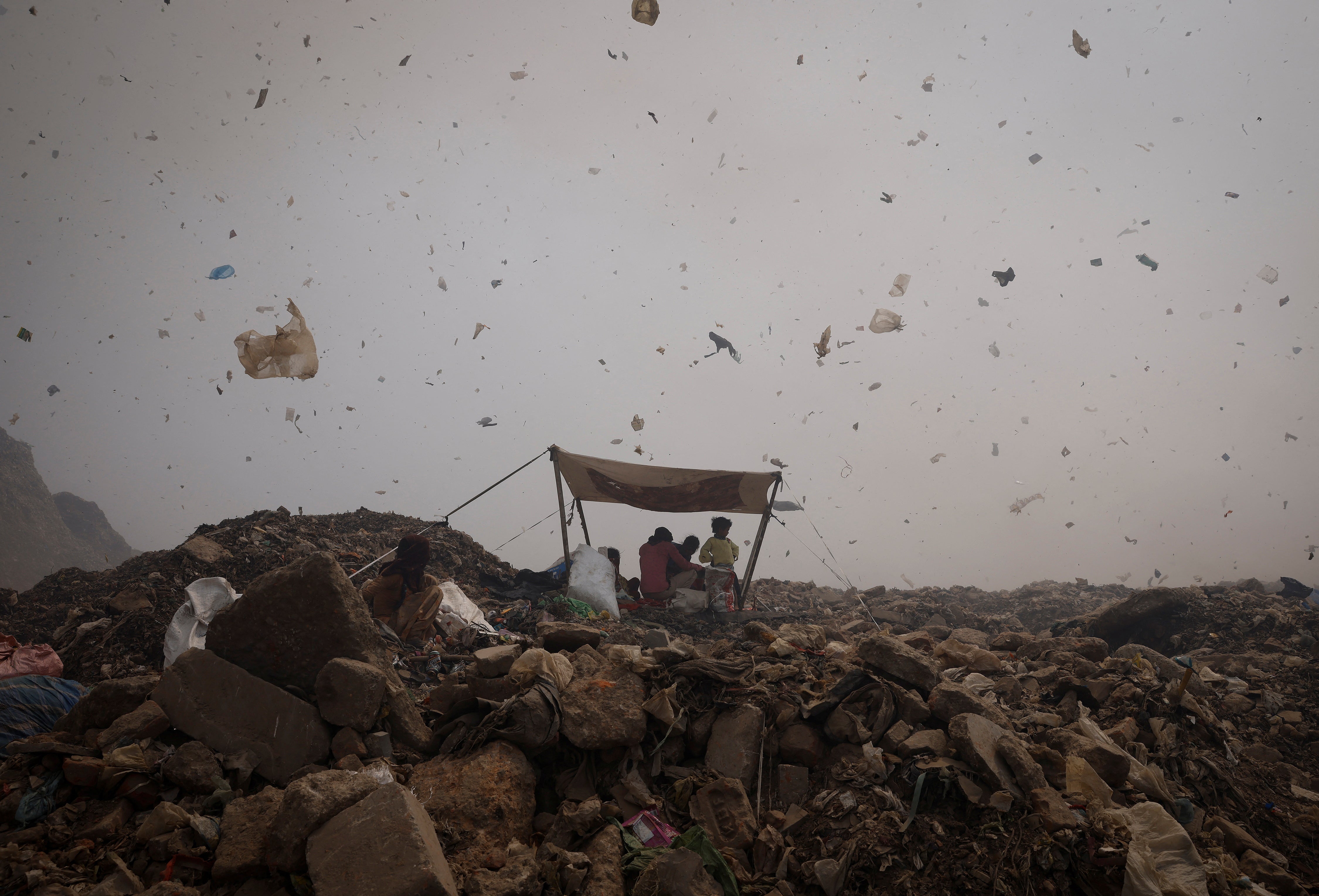 Waste collectors take shelter from the heat under a tarpaulin as debris and smoke billow from a fire at a landfill site in New Delhi