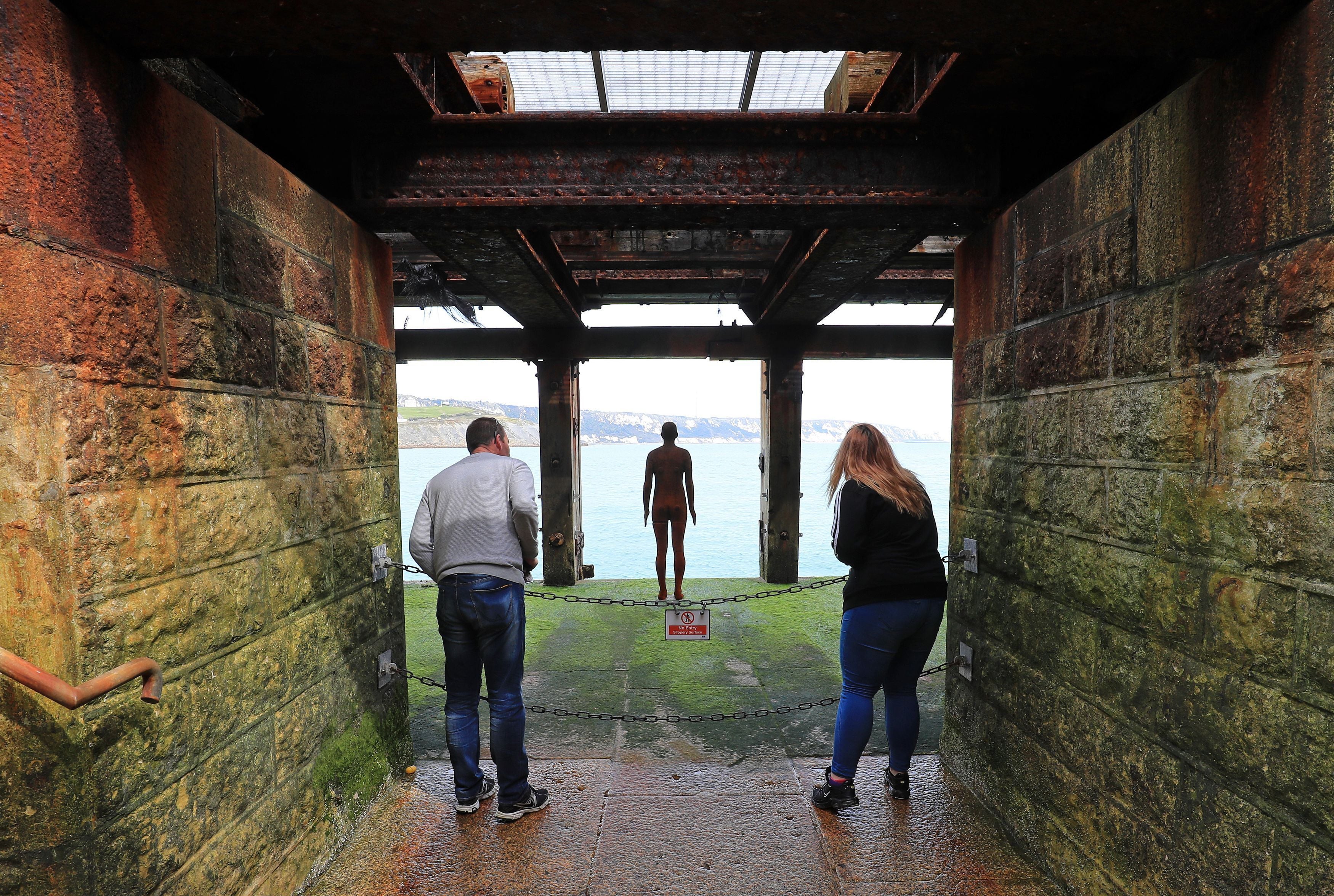 Visitors look at a piece by Antony Gormley called ‘Another Time XVIII 2013’ under Folkestone harbour