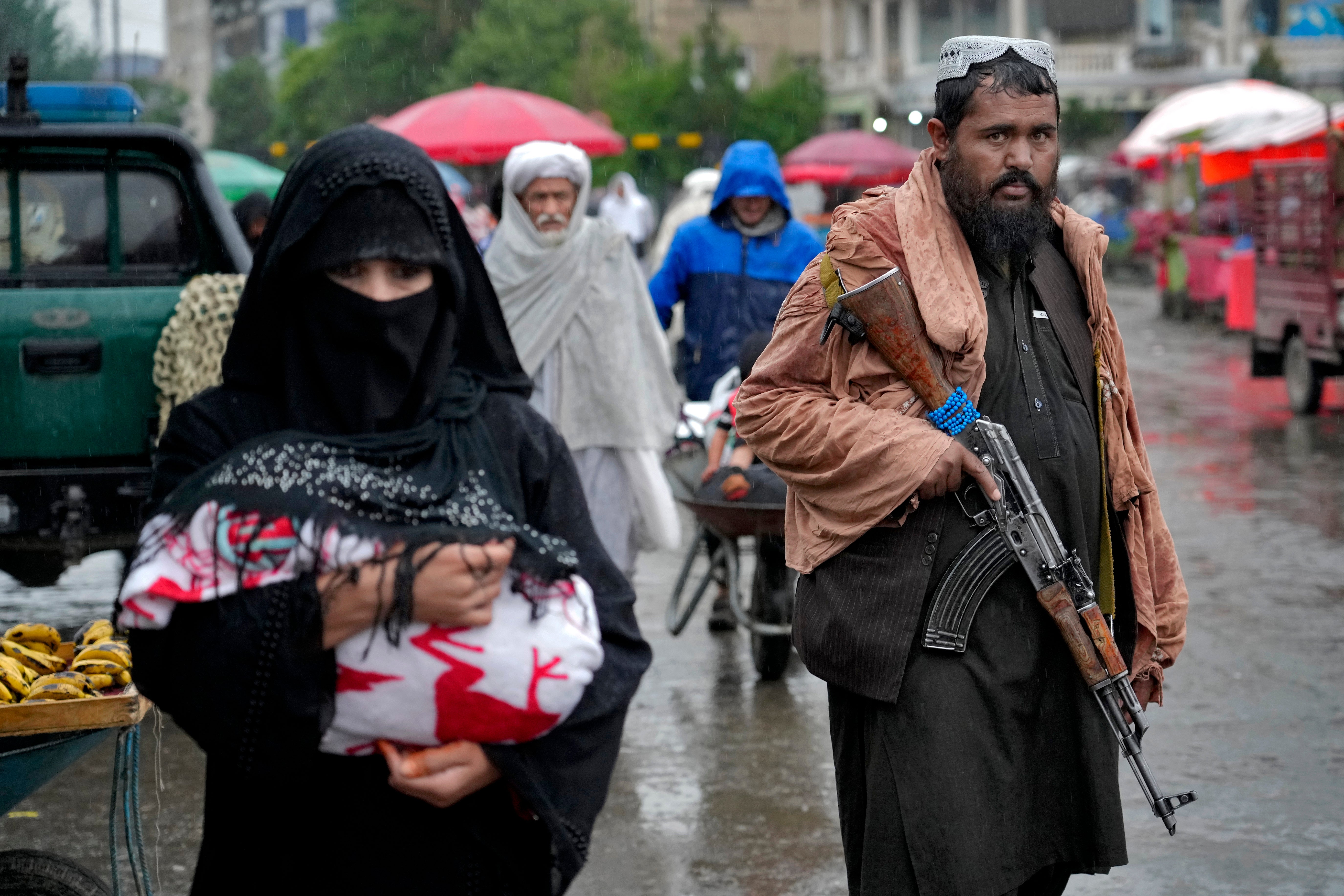 A Taliban fighter stands guard as people walk through the old market in the city of Kabul