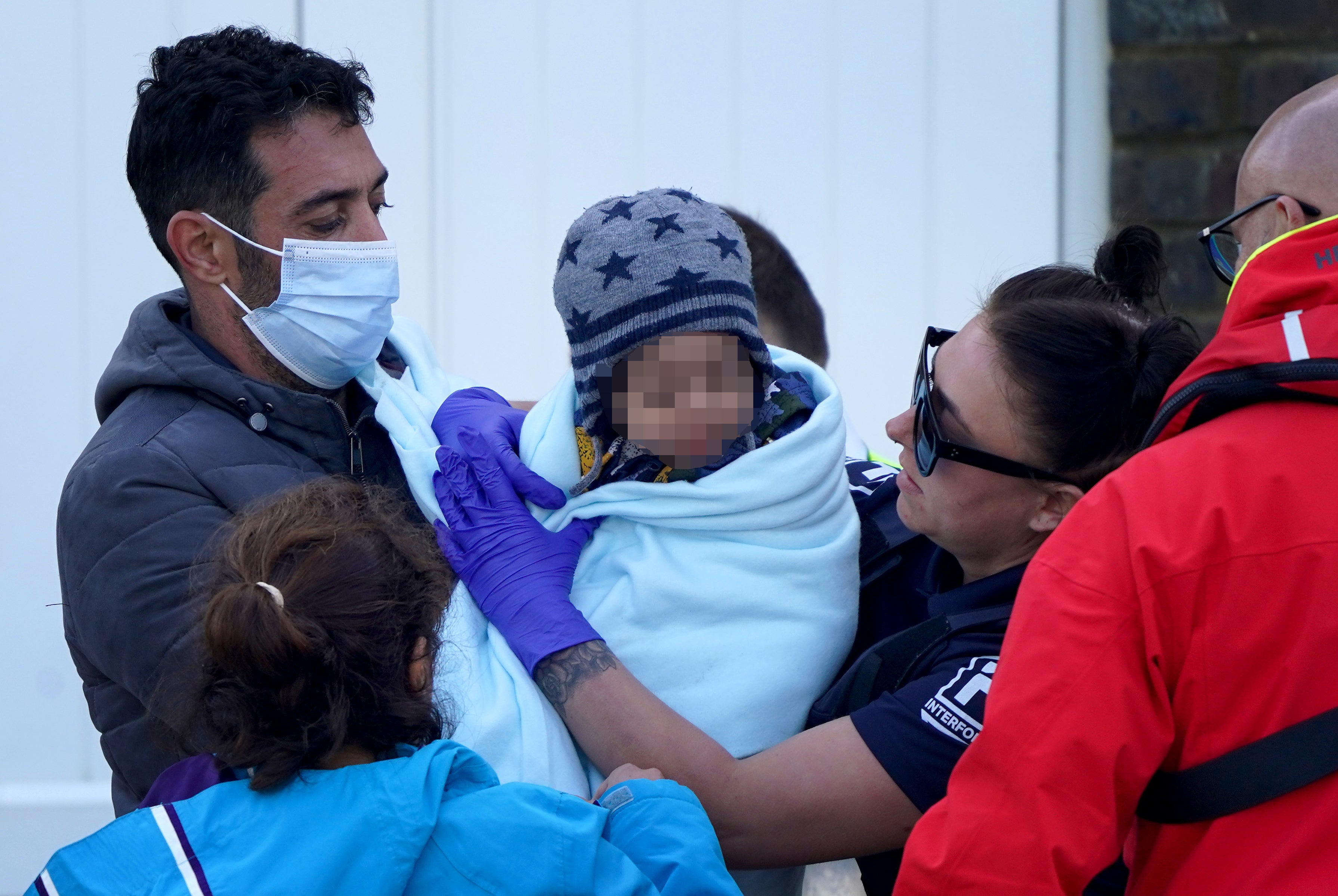 A young child wrapped in a blanket is among a group of people thought to be migrants brought in to Dover, Kent