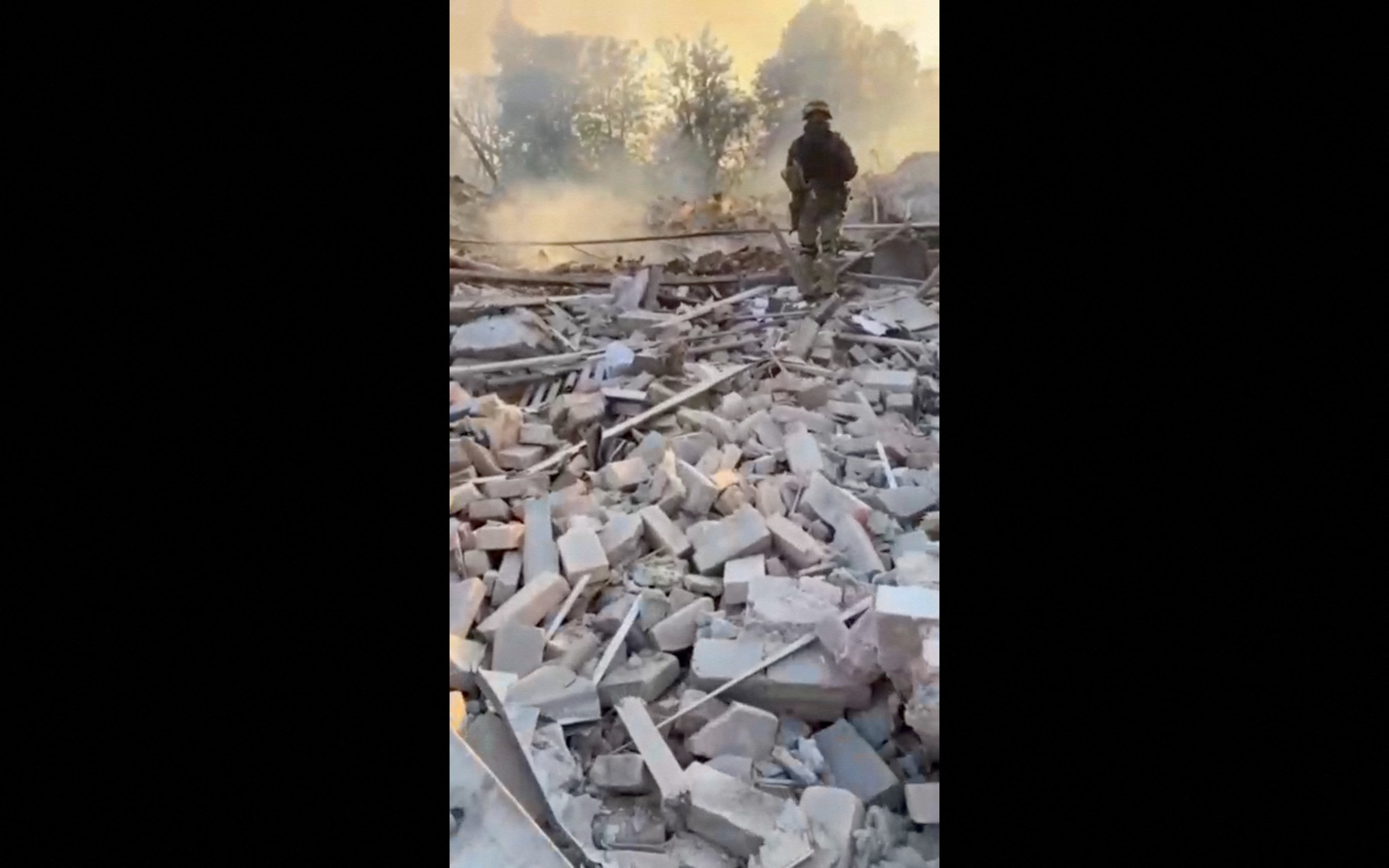 A man wearing military uniform stands on top of rubble in Bilohorivka