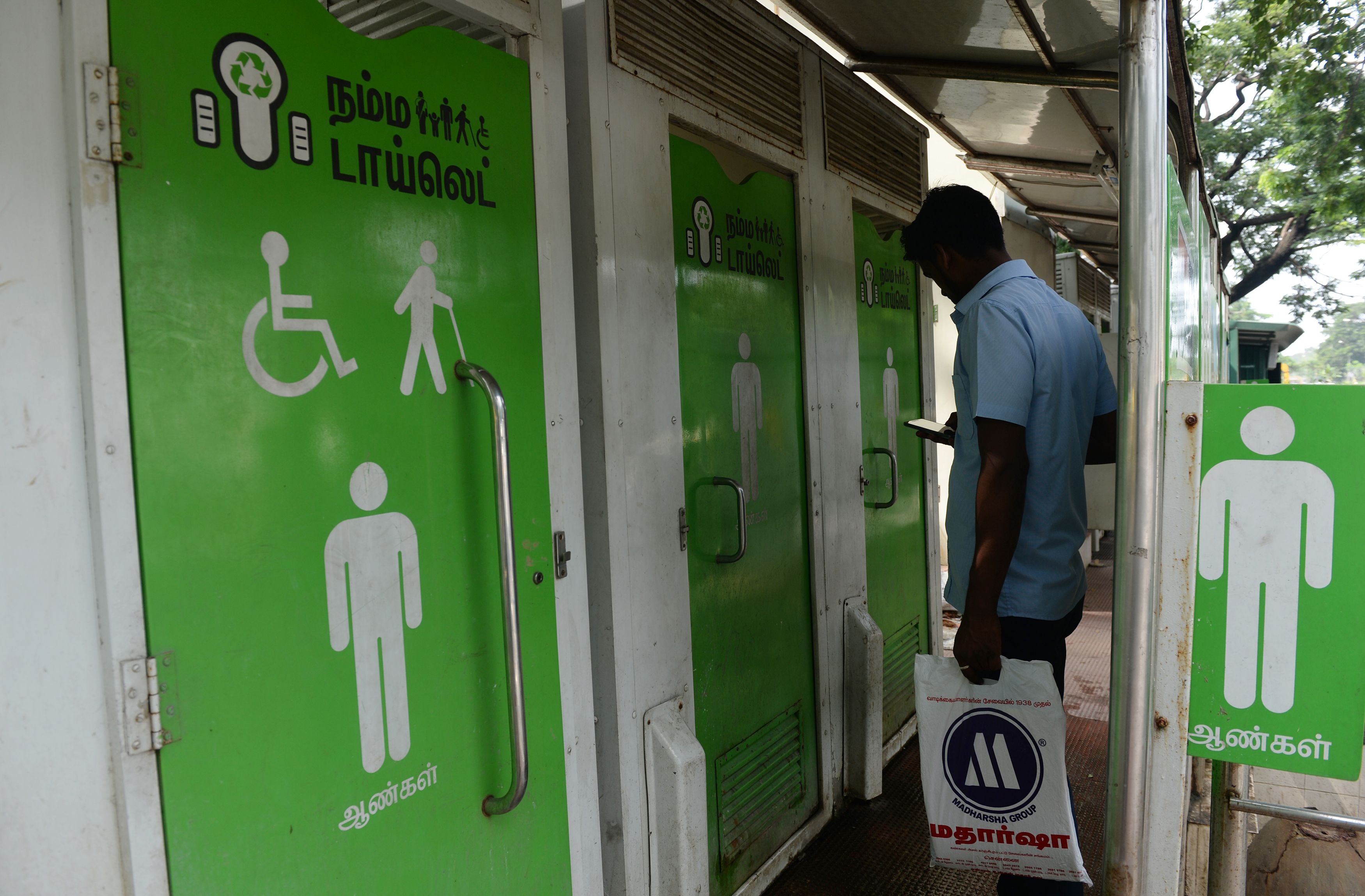 A man checks his phone as he waits to use a public toilet on a street in Chennai