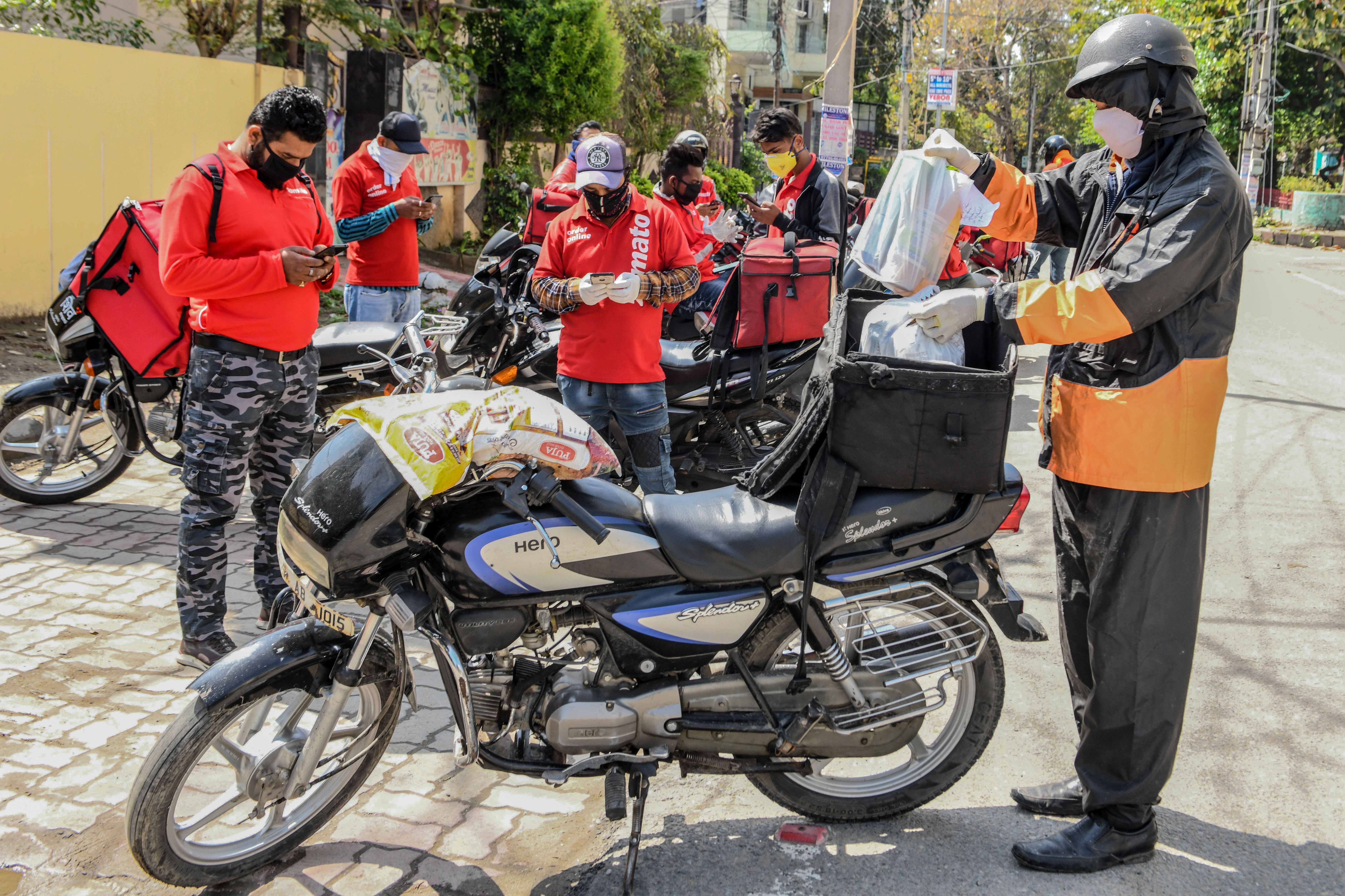 In Amritsar, a Swiggy delivery man (R) wearing a face-covering puts food in a bag tied to his motorbike as Zomato delivery men check their mobile phones in the background