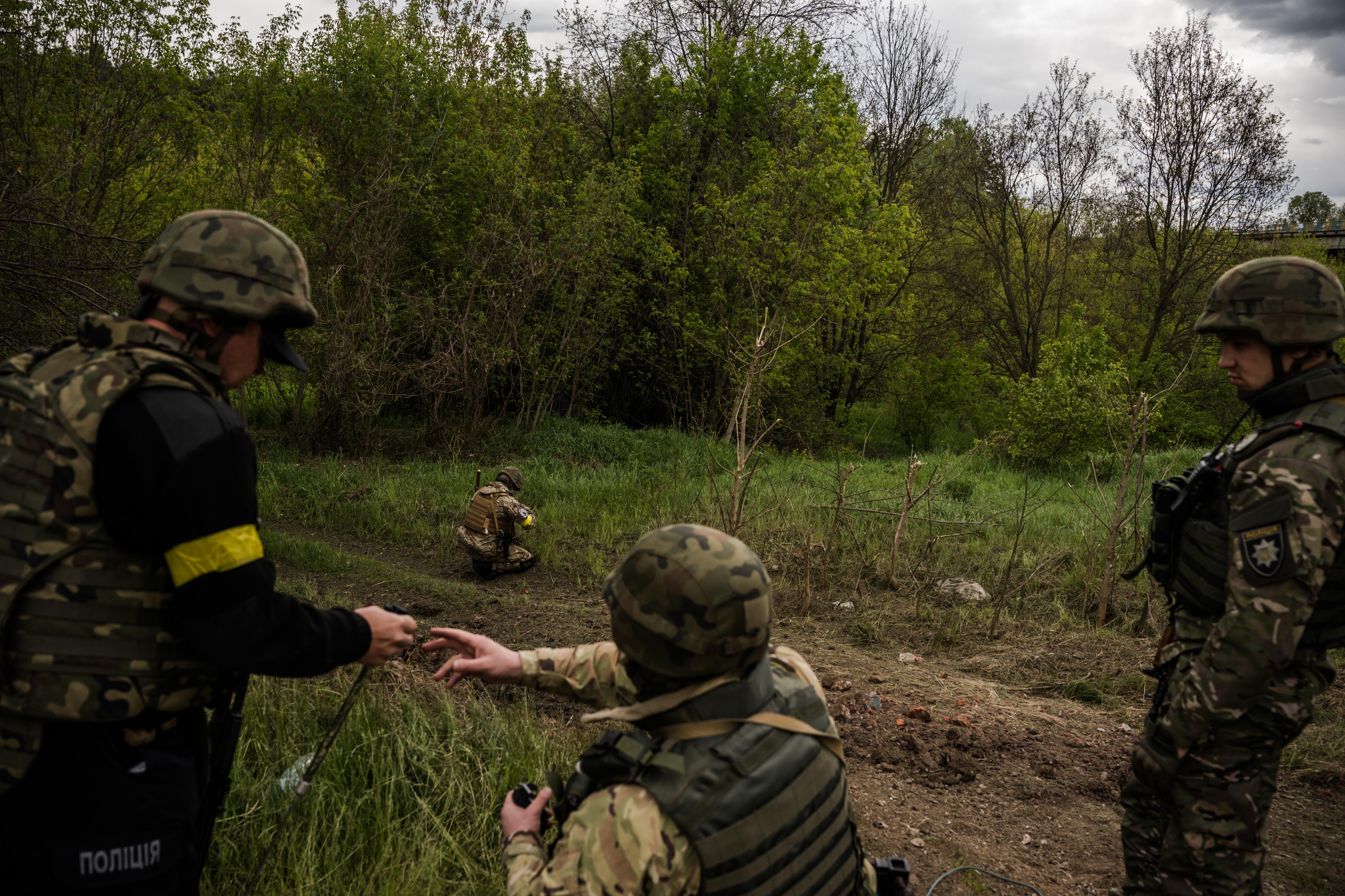 A Kharkiv police de-mining team clears a path to the bodies of two women killed by a blast near Tsyrkuny