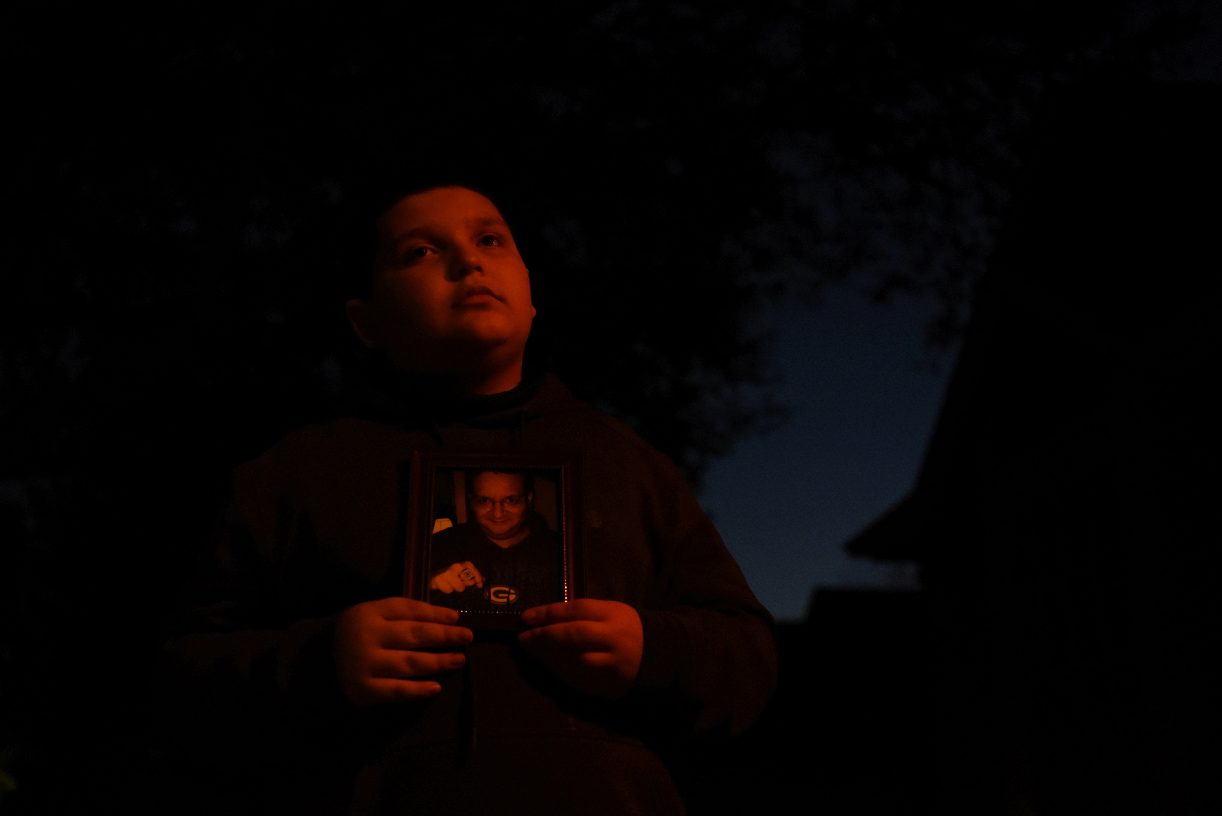 Aidan Garza poses for a portrait holding a photograph of his father, David Garza