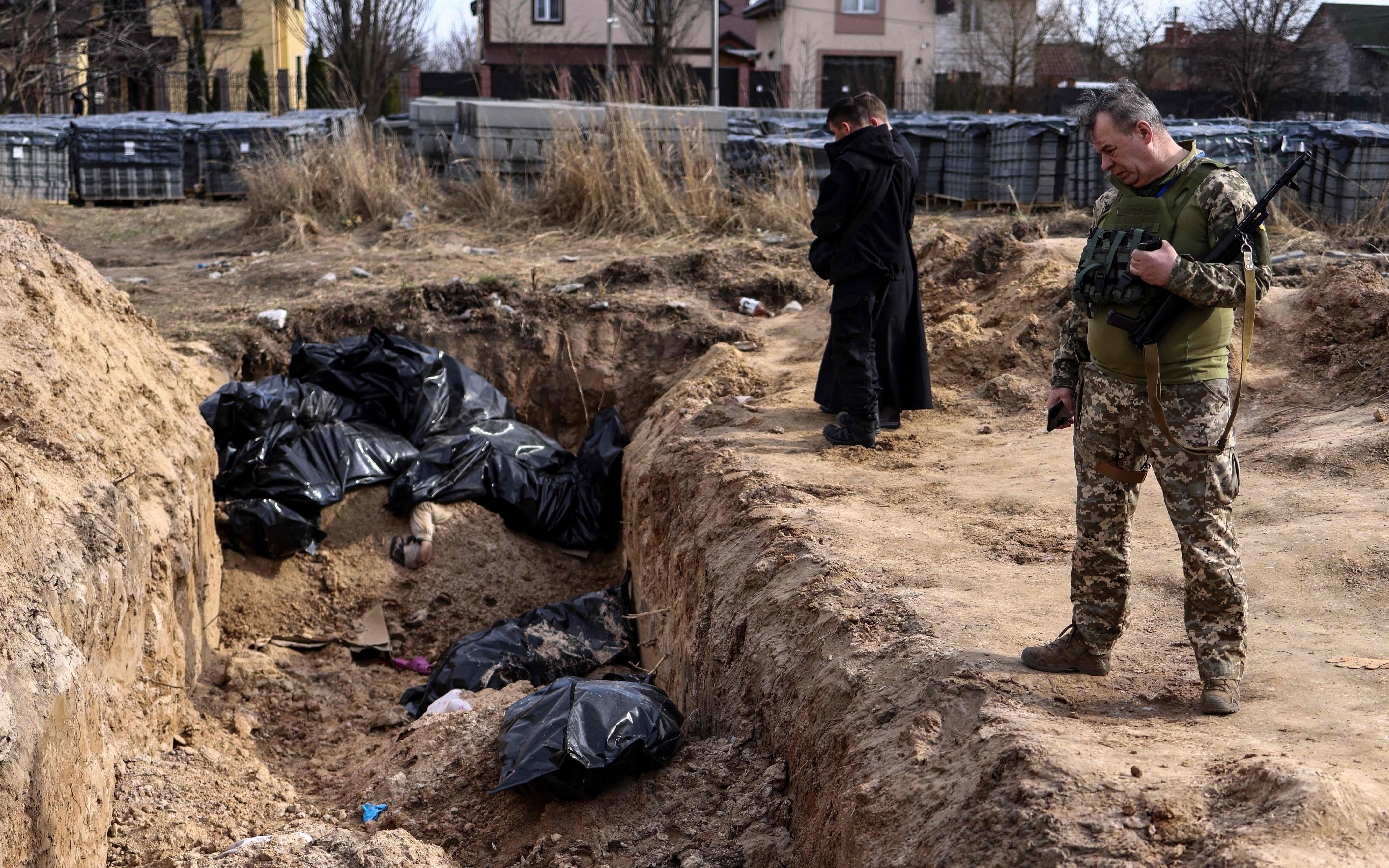 A Ukranian soldier looks at body bags as priests pray at a mass grave in the grounds surrounding St Andrew’s Church in Bucha