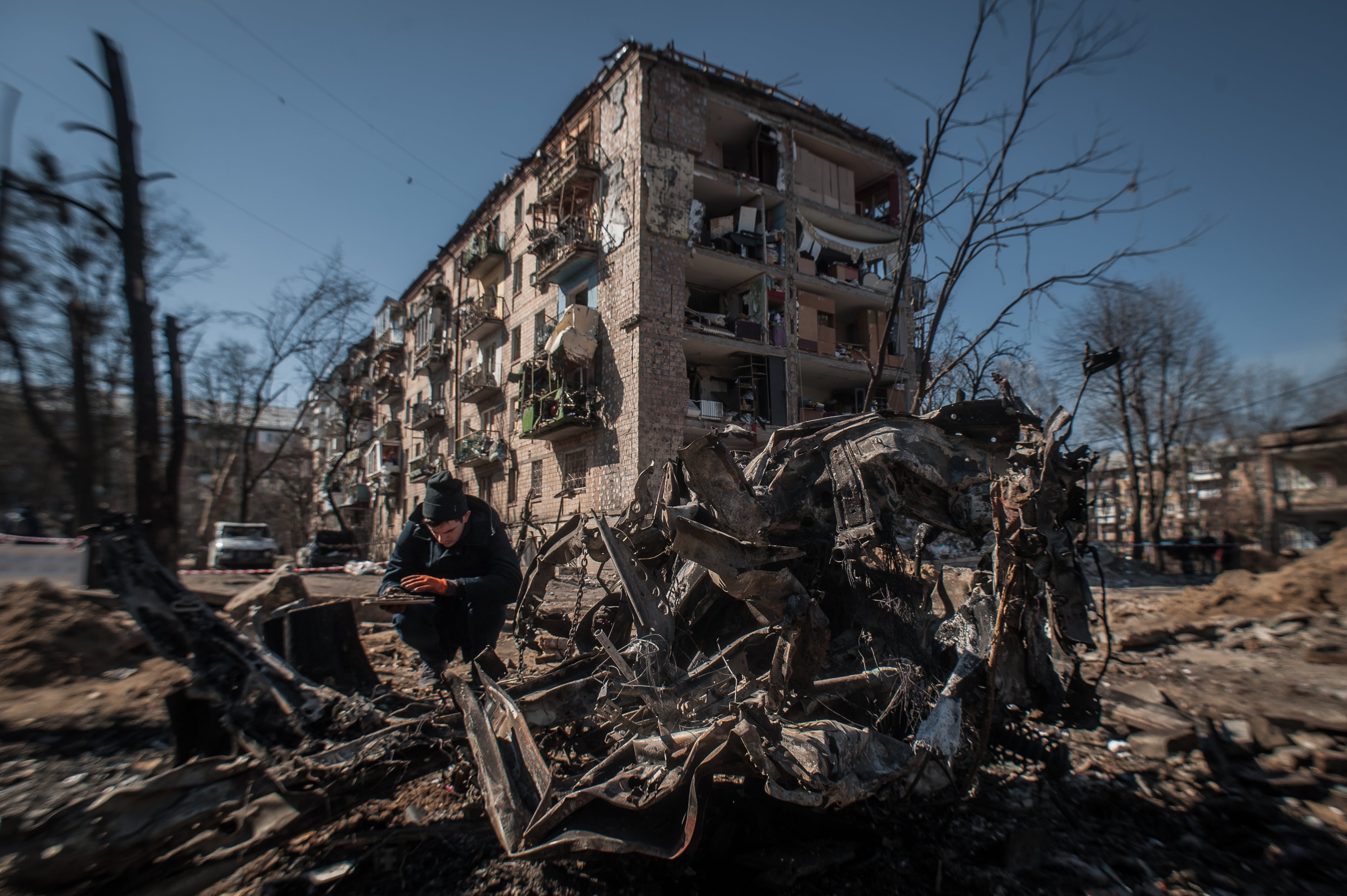 A man disassembles parts of a burned car near the destroyed houses in Kyiv