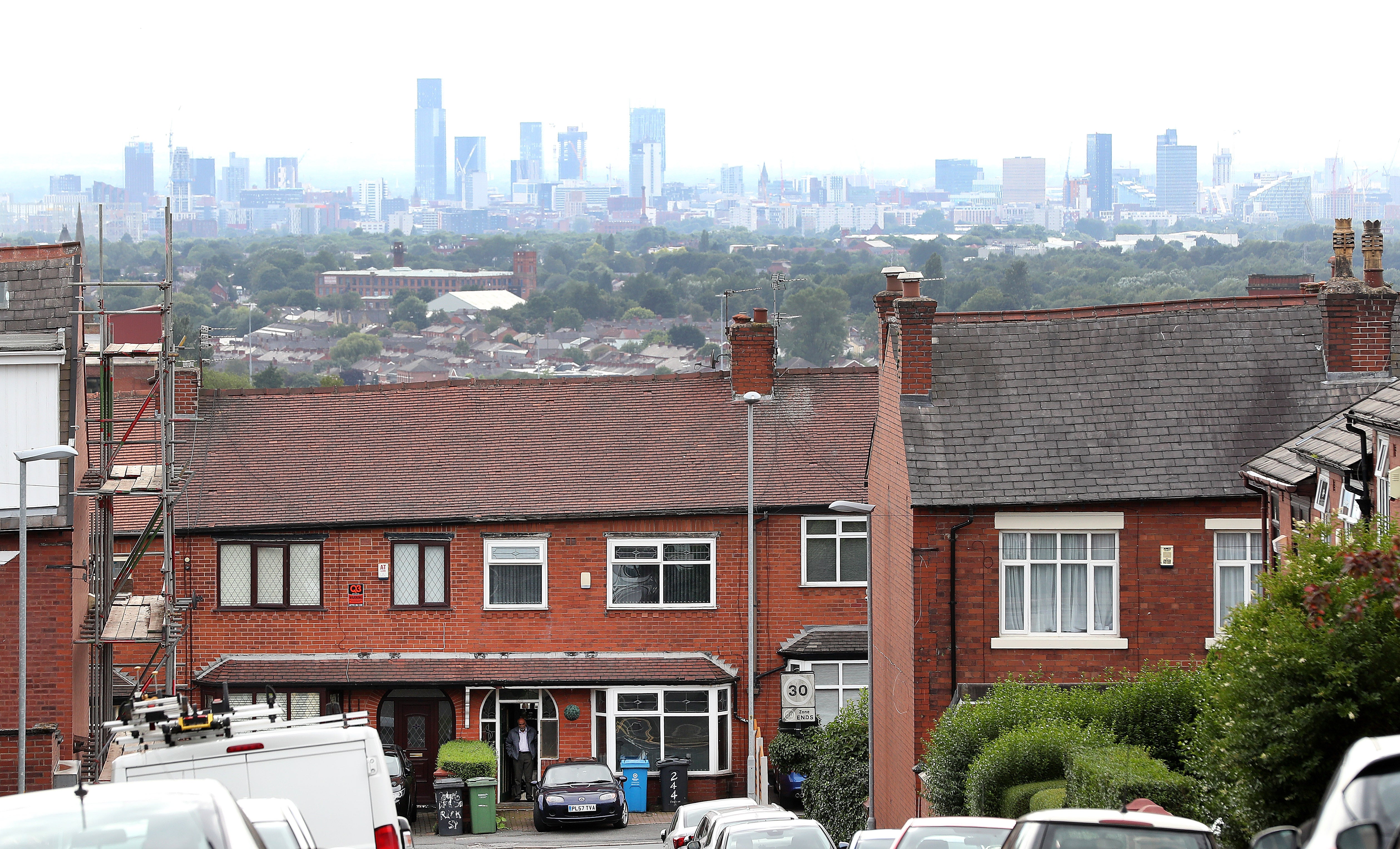 A Resident in Oldham stands in his doorway with the Manchester skyline behind (Martin Rickett/PA)