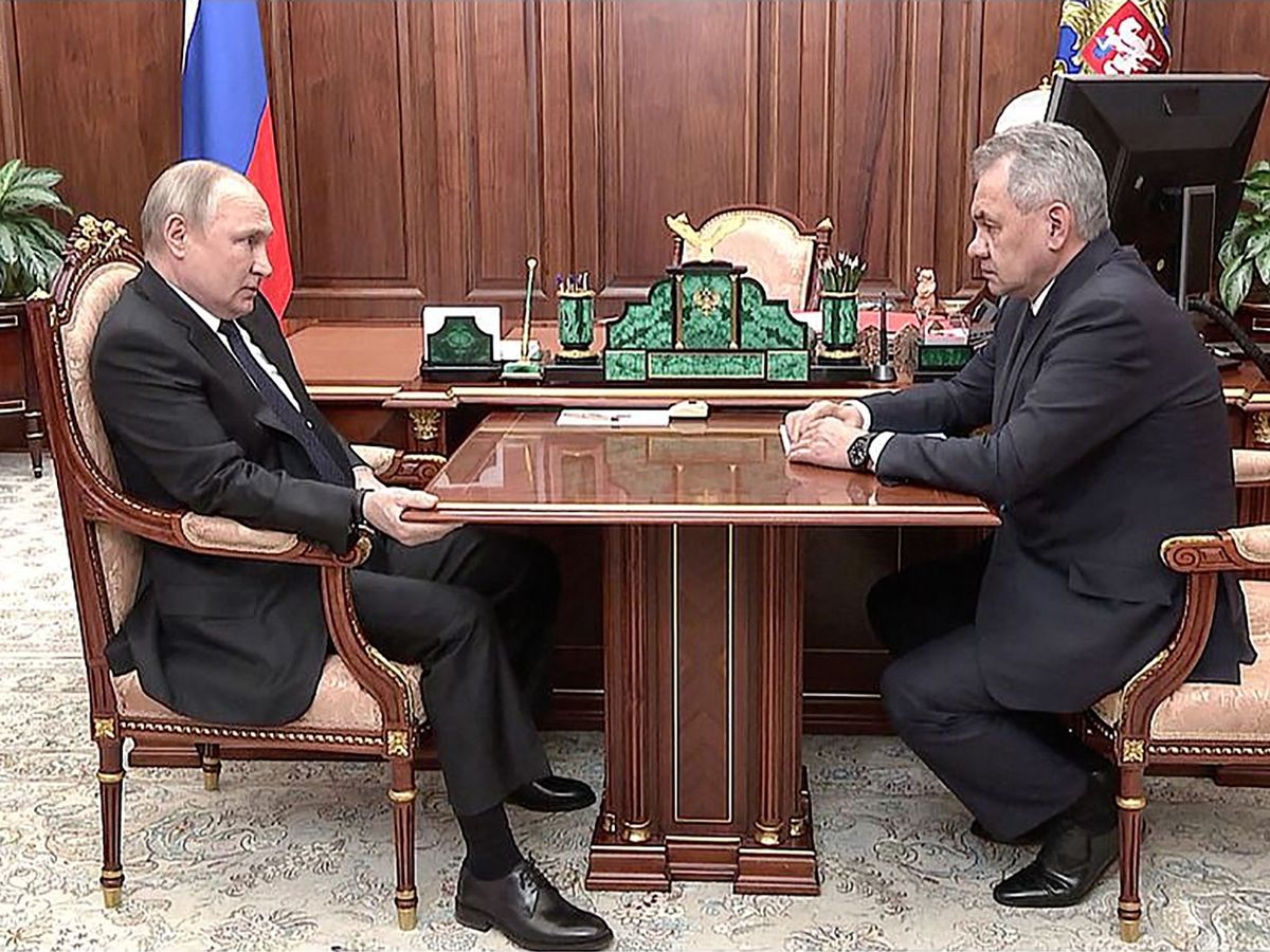 Vladimir Putin awkwardly grips a table during a meeting with his defence minister