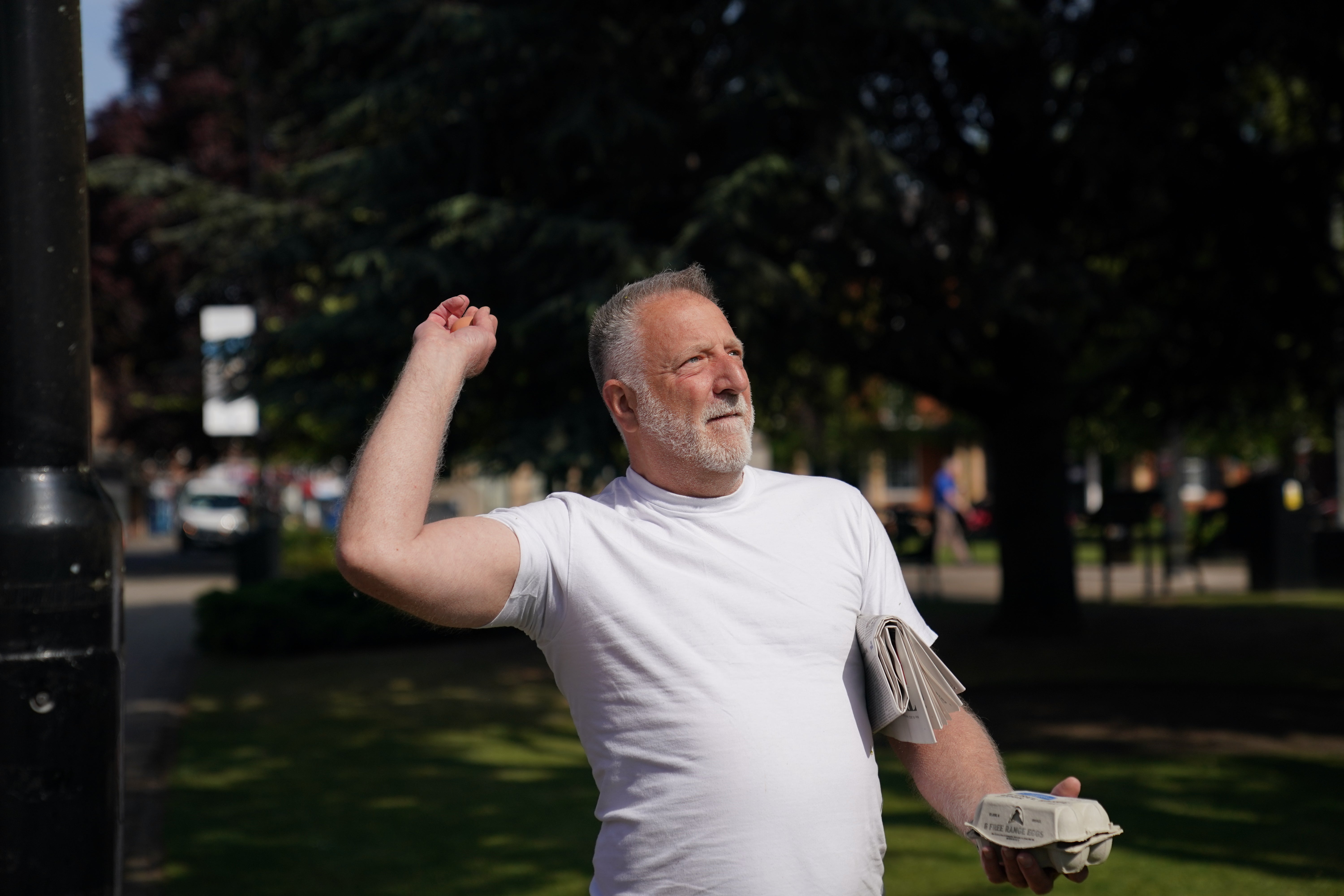 A man in a white t-shirt throws eggs at a statue of Thatcher