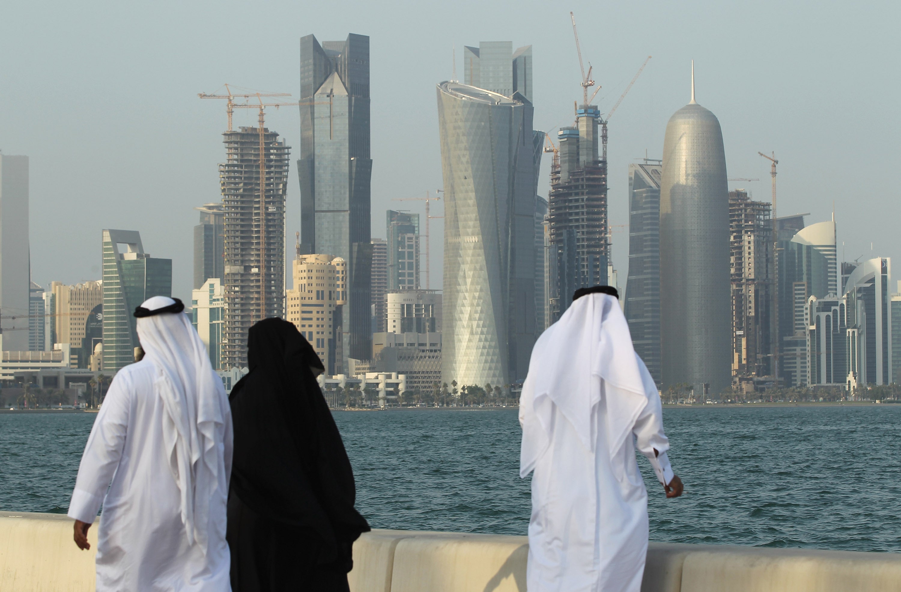 Men and women wearing traditional Qatari clothing walk along the Corniche in Doha