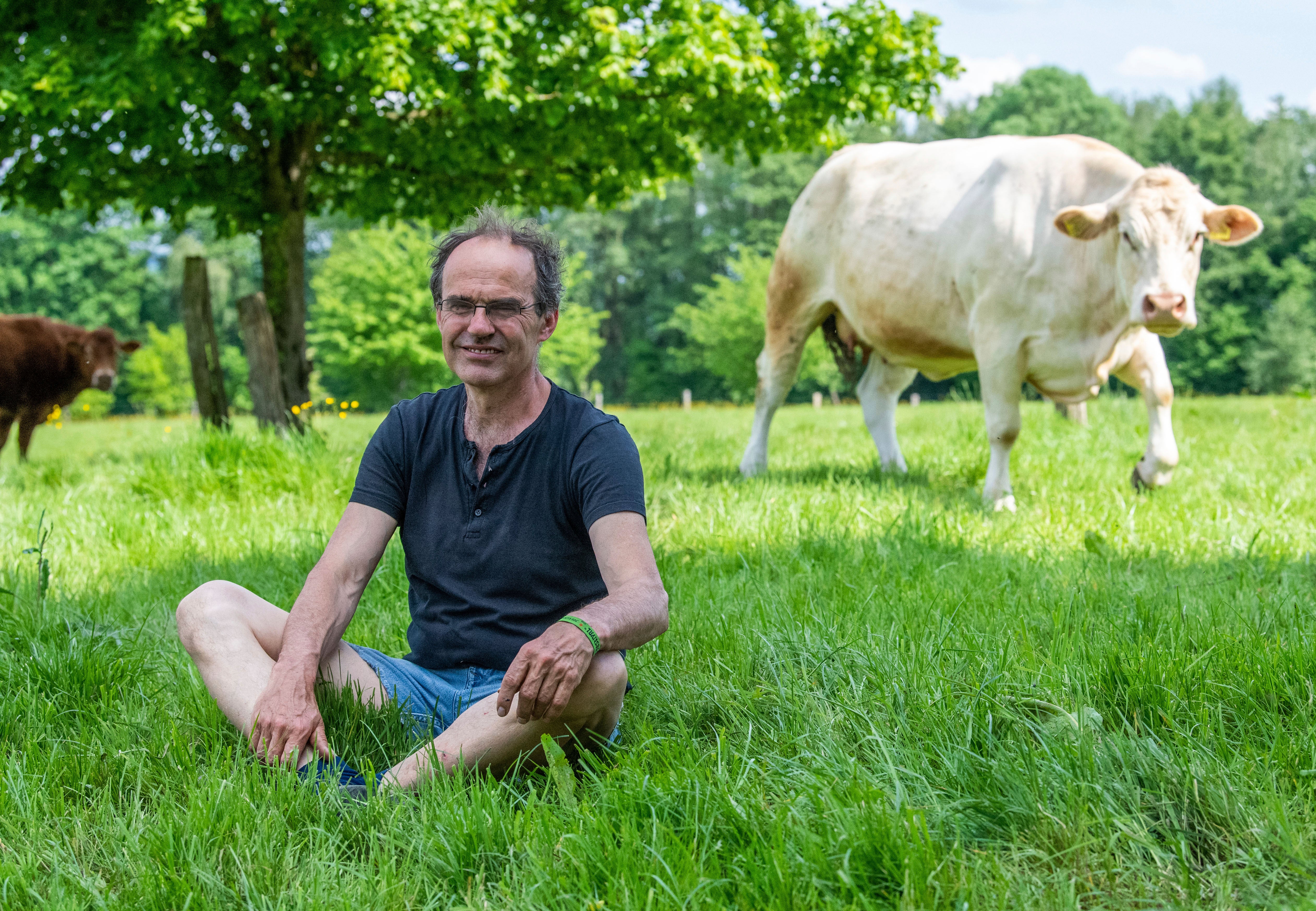 Allhoff-Cramer sits in a pasture next to one of his cows in Detmold, Germany