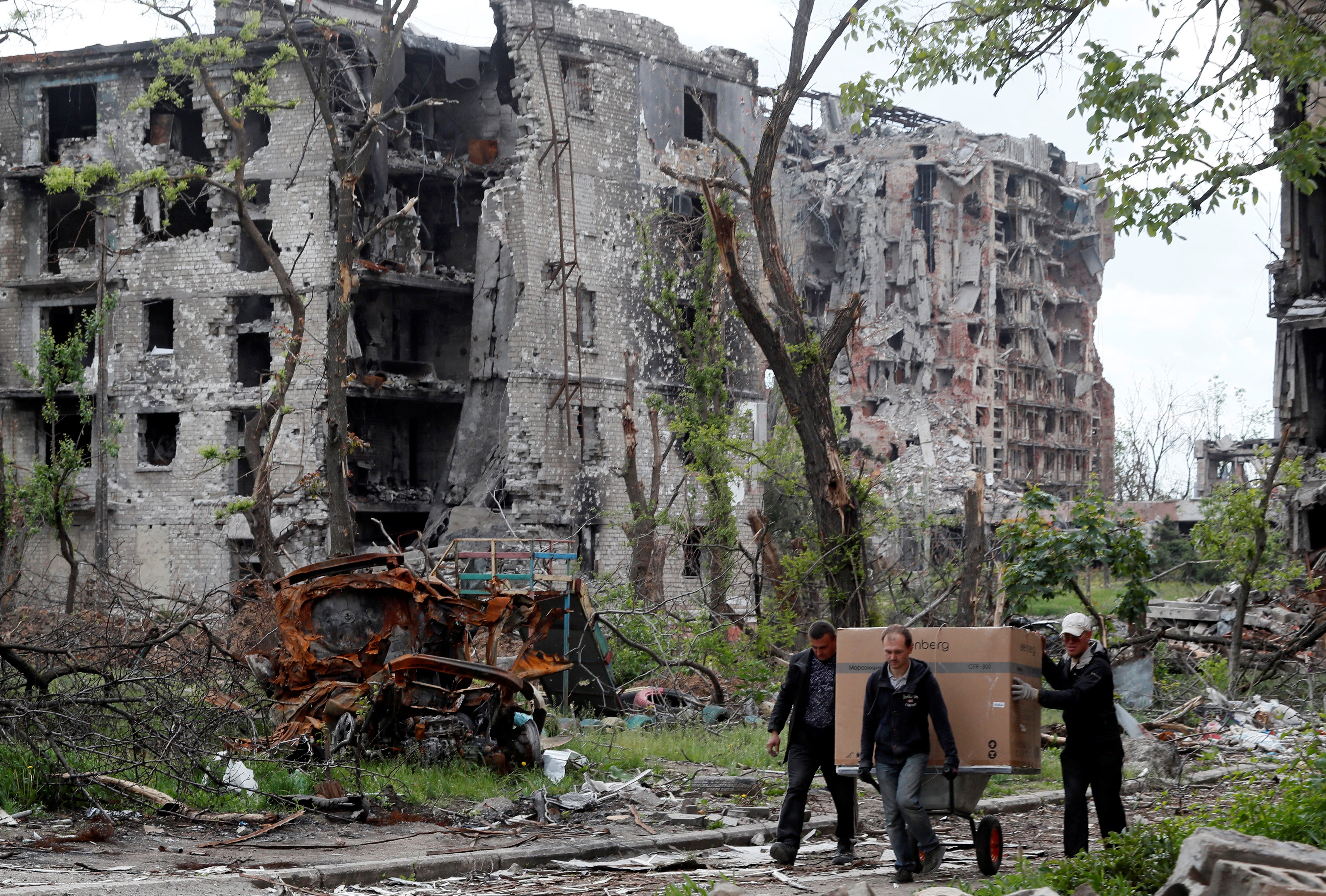 Local residents transport a box on a wheelbarrow past a heavily damaged apartment building near Azovstal Iron and Steel Works, during Ukraine-Russia conflict in the southern port city of Mariupol