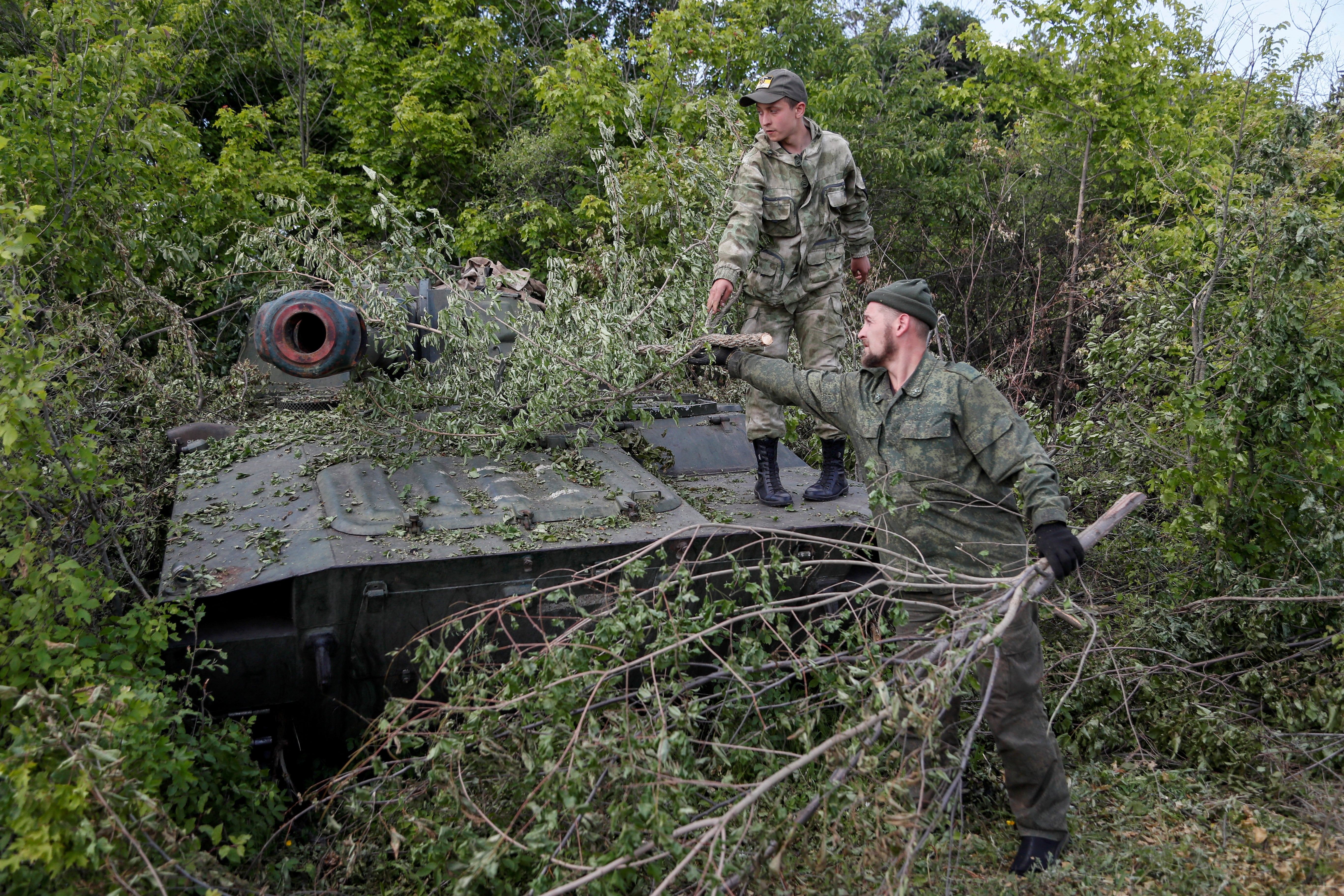 Pro-Russian troops remove branches covering a self-propelled howitzer in Luhansk region on Tuesday