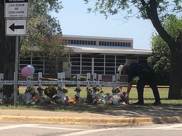 A law enforcement officer lays flowers brought by locals - who were not allowed beyond a certain point as officials prepared for a Thursday press conference - at the memorial outside of Robb Elementary School in Uvalde