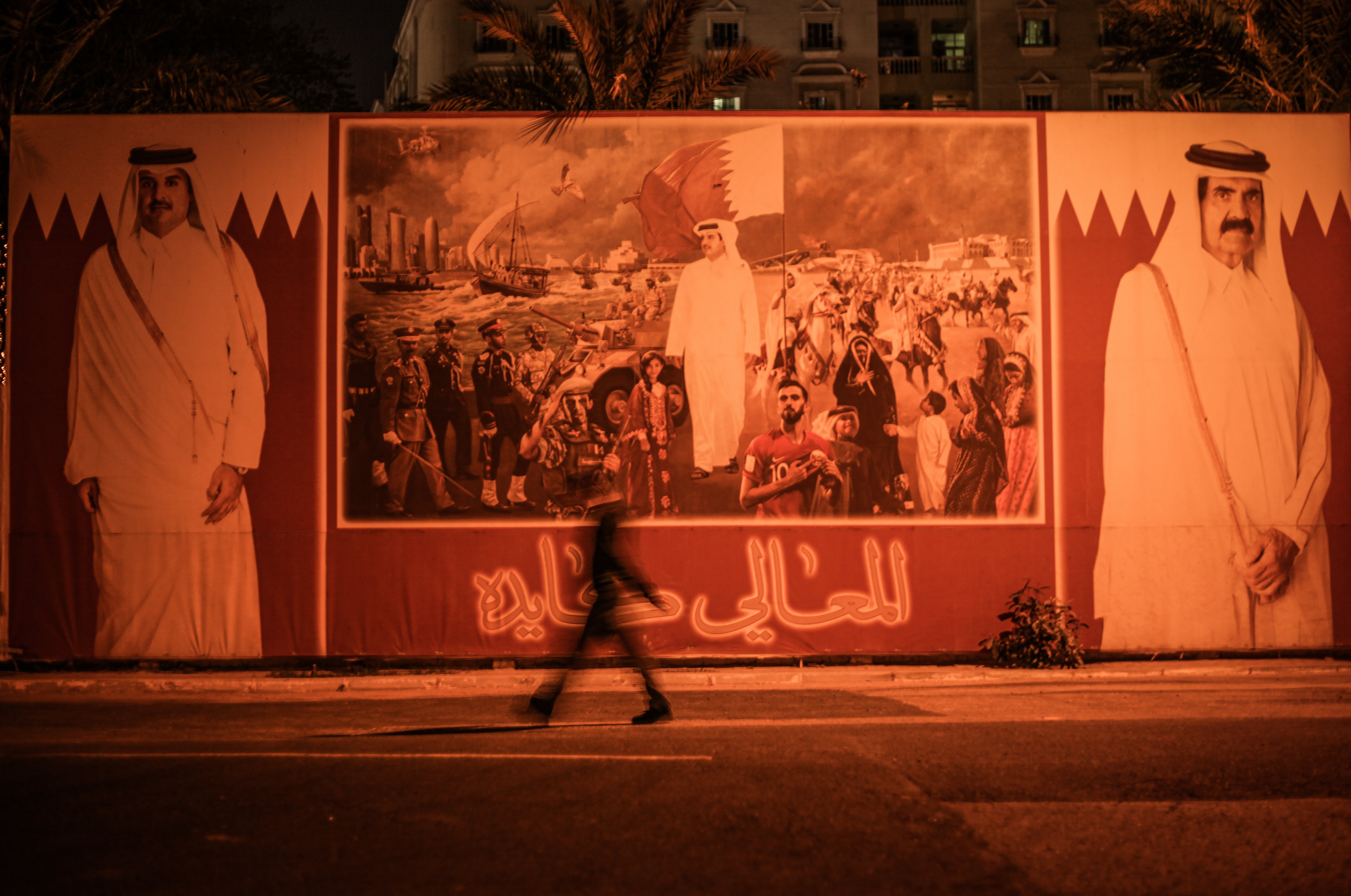 A person walks past a board showing the Emir of Qatar and his father