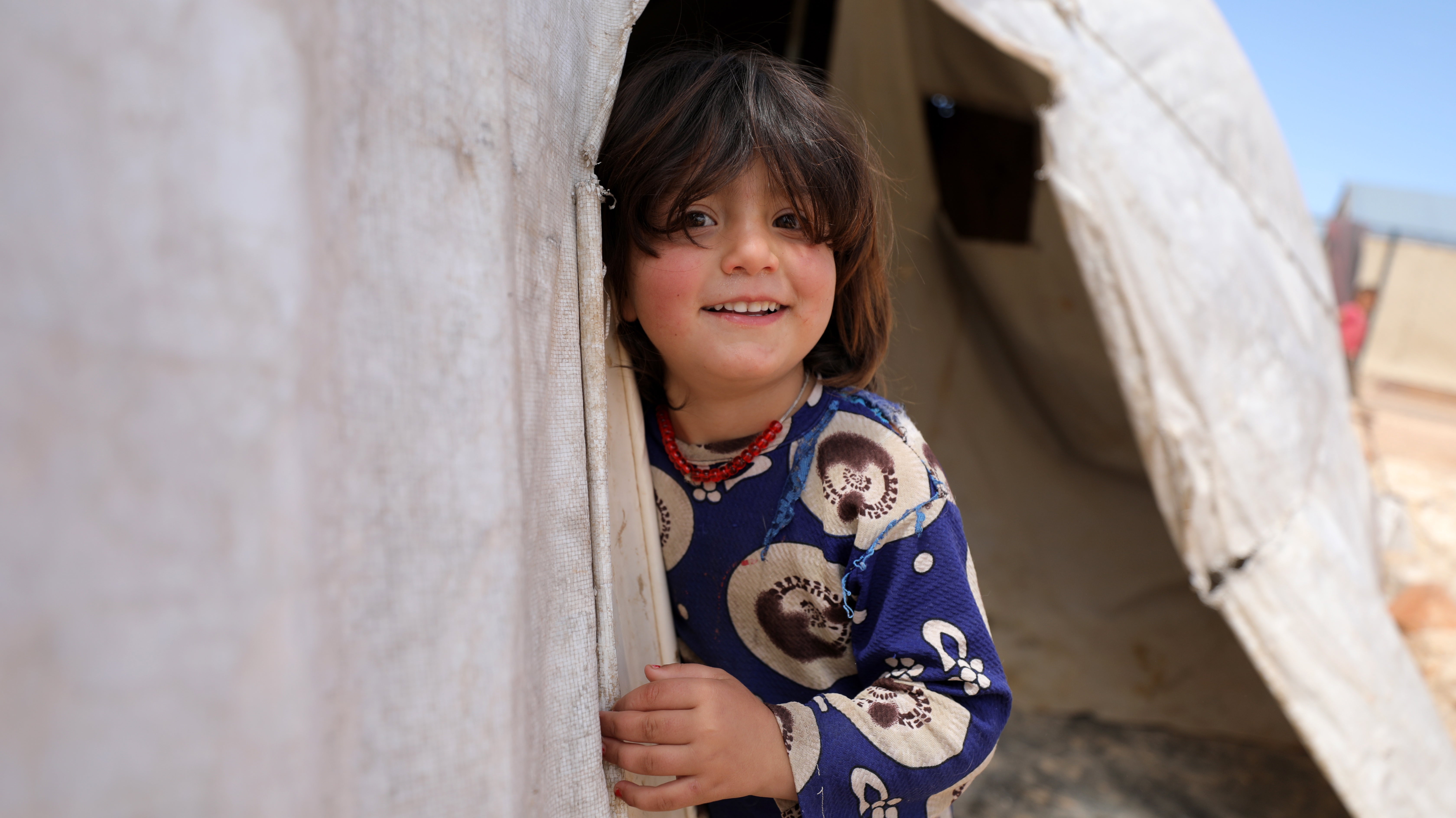 A child poses for a photo from a makeshift shelter at Al-Tehh camp for Syrians in Idlib