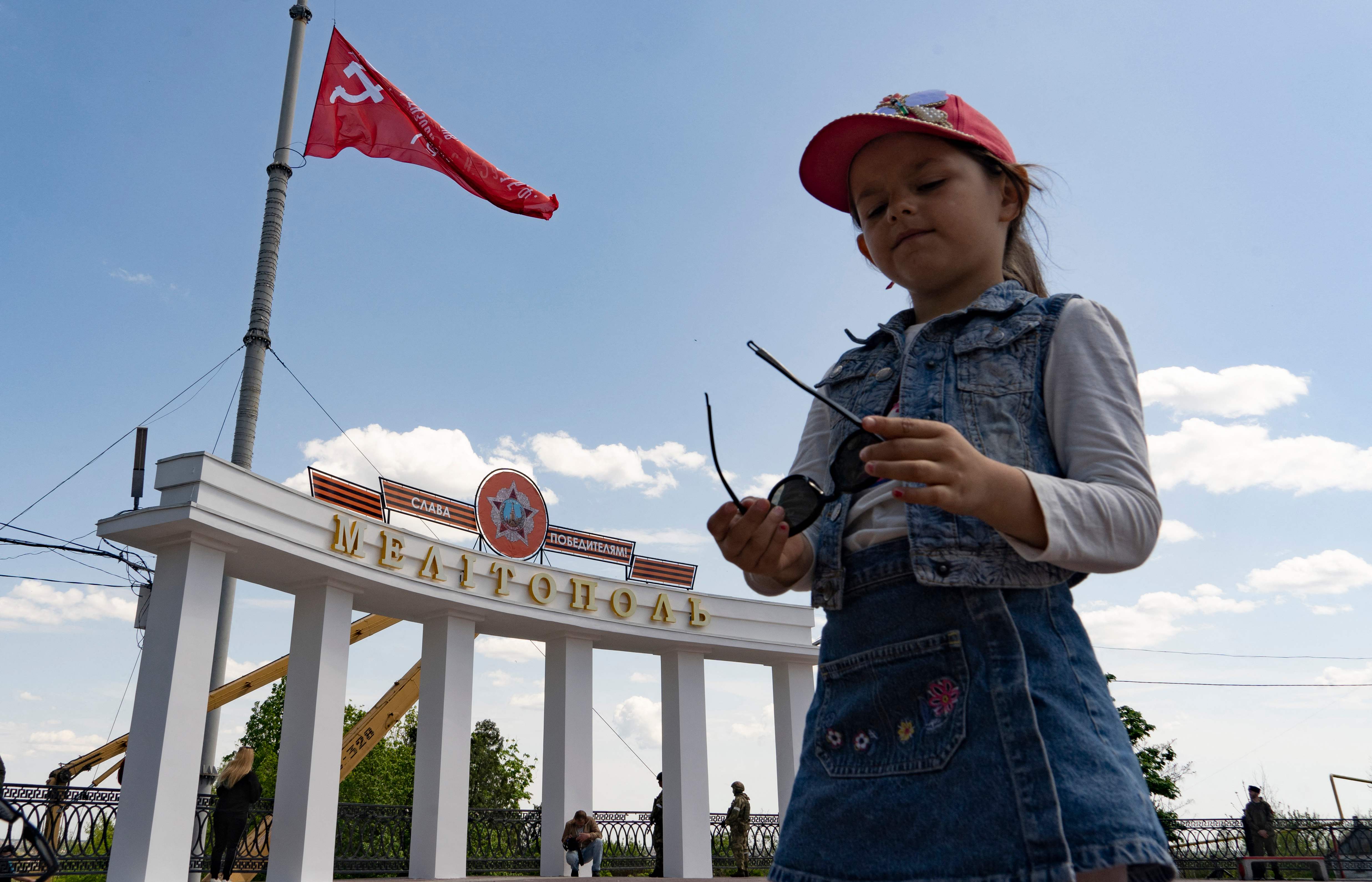 A girl stands near the Melitopol arch decorated with a red flag, St George ribbon and Soviet Second World War-era medal with the slogan ‘Glory to the victors!’