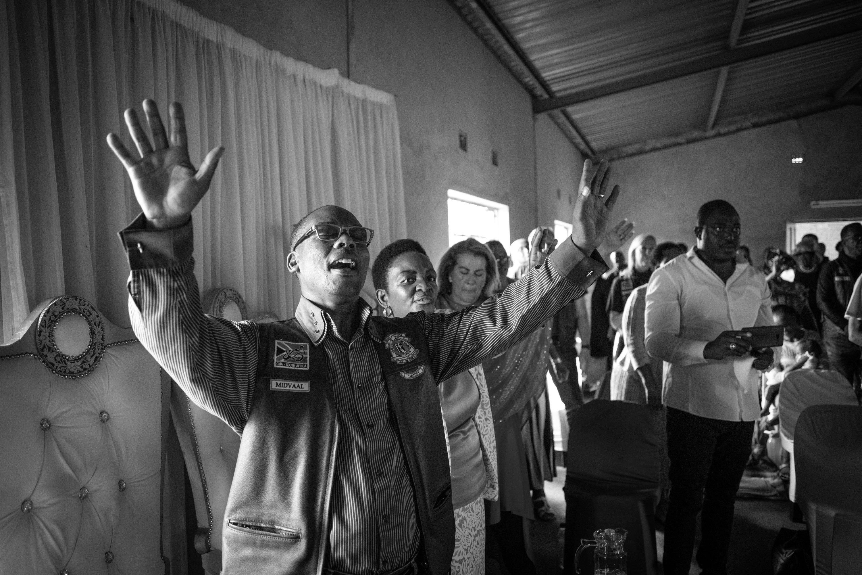 Newly patched CMA member, Pastor Doctor Danny Molapisi (left), raises his arms in prayer at his local community church in the Sebokeng township