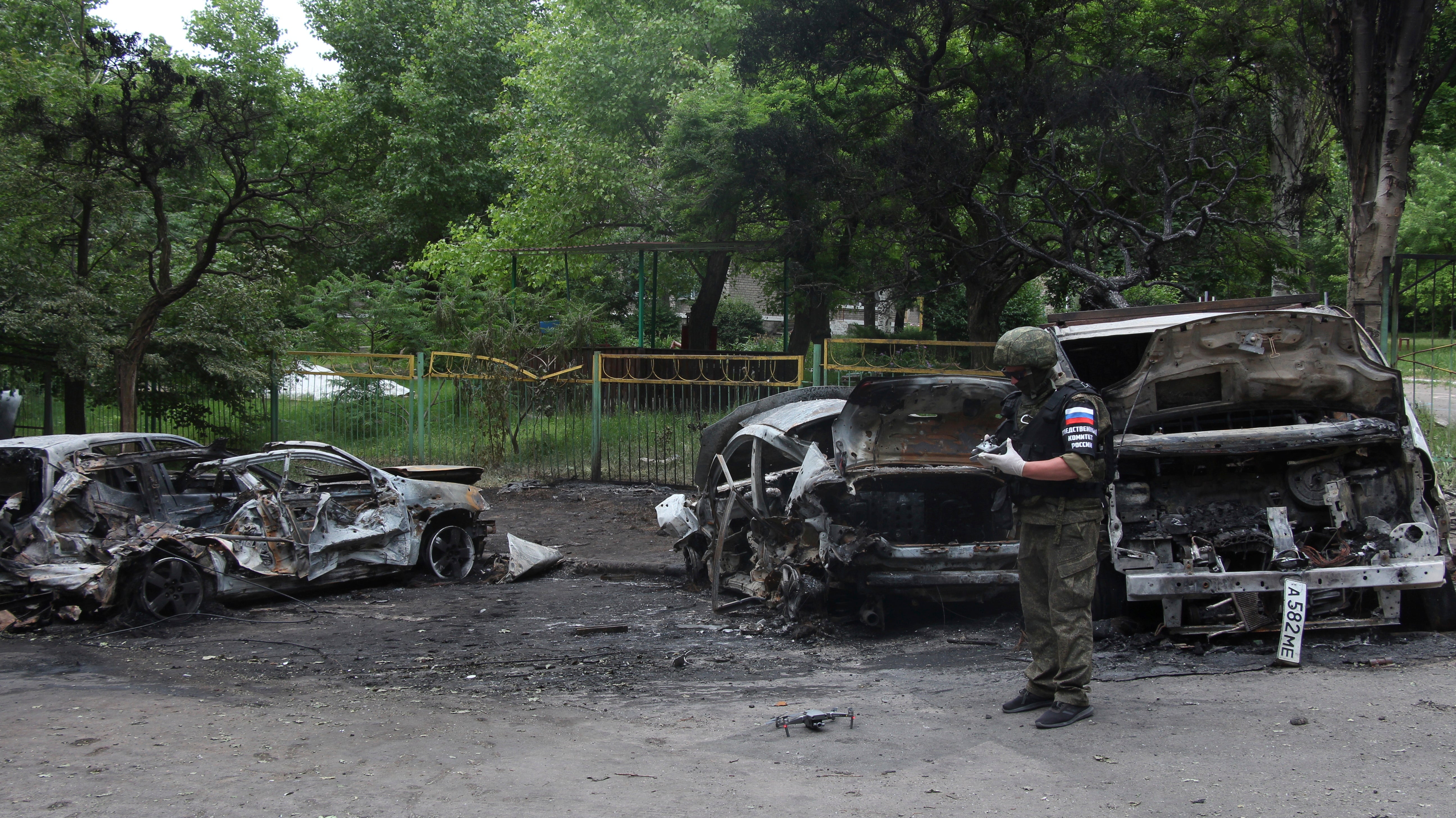 A member of Russian Investigative Committee prepares to use a drone at the scene of burned vehicles after the shelling in the Petrovsky district of Donetsk