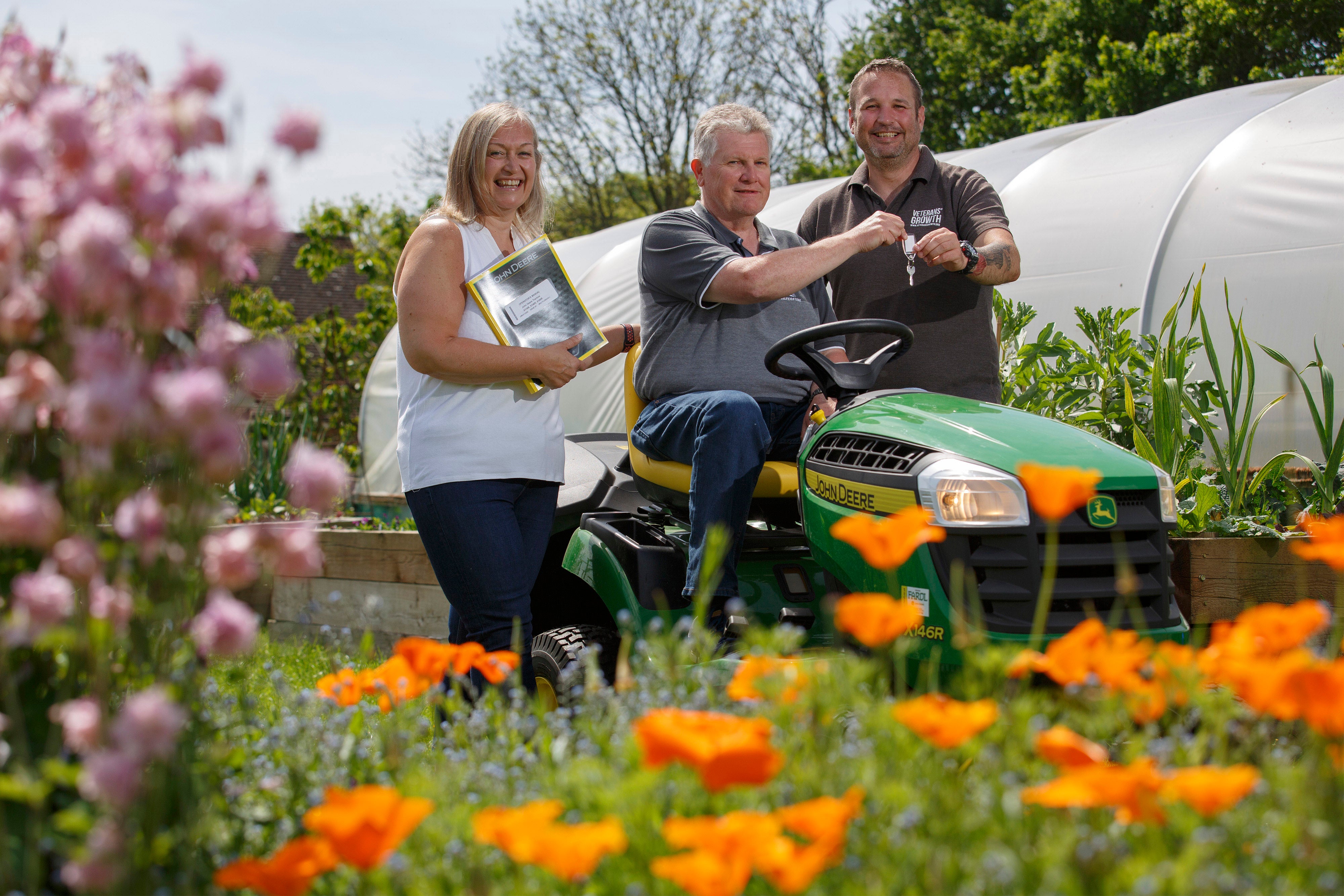 Jason Stevens, right, Veterans Growth CEO, is presented with a ride-on mower from lottery winners David and Donna Stickley(Luke MacGregor/Camelot/PA)