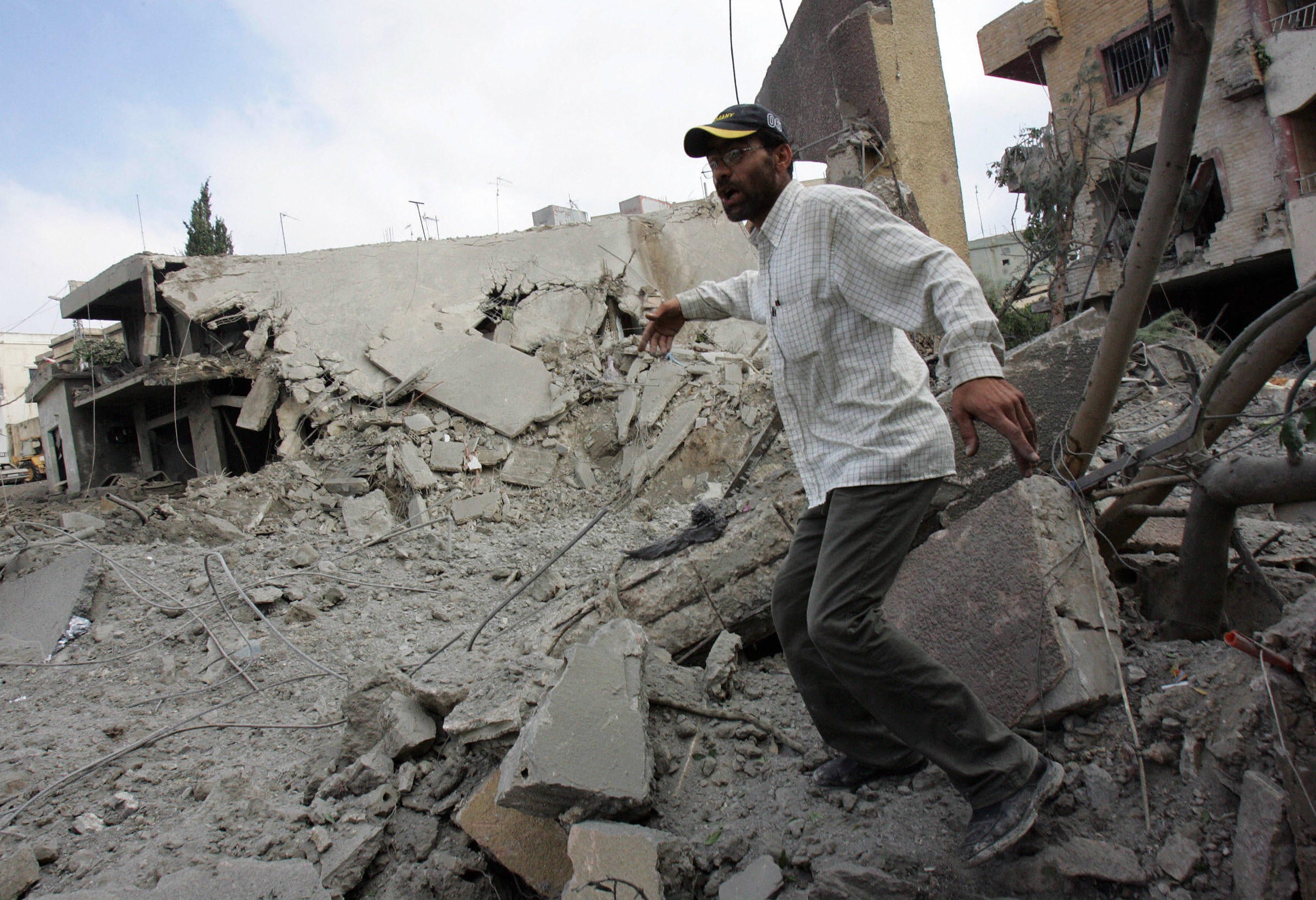 A Lebanese man runs to prevent photographers from taking pictures of a Hezbollah building destroyed in an Israeli airstrike in Qana