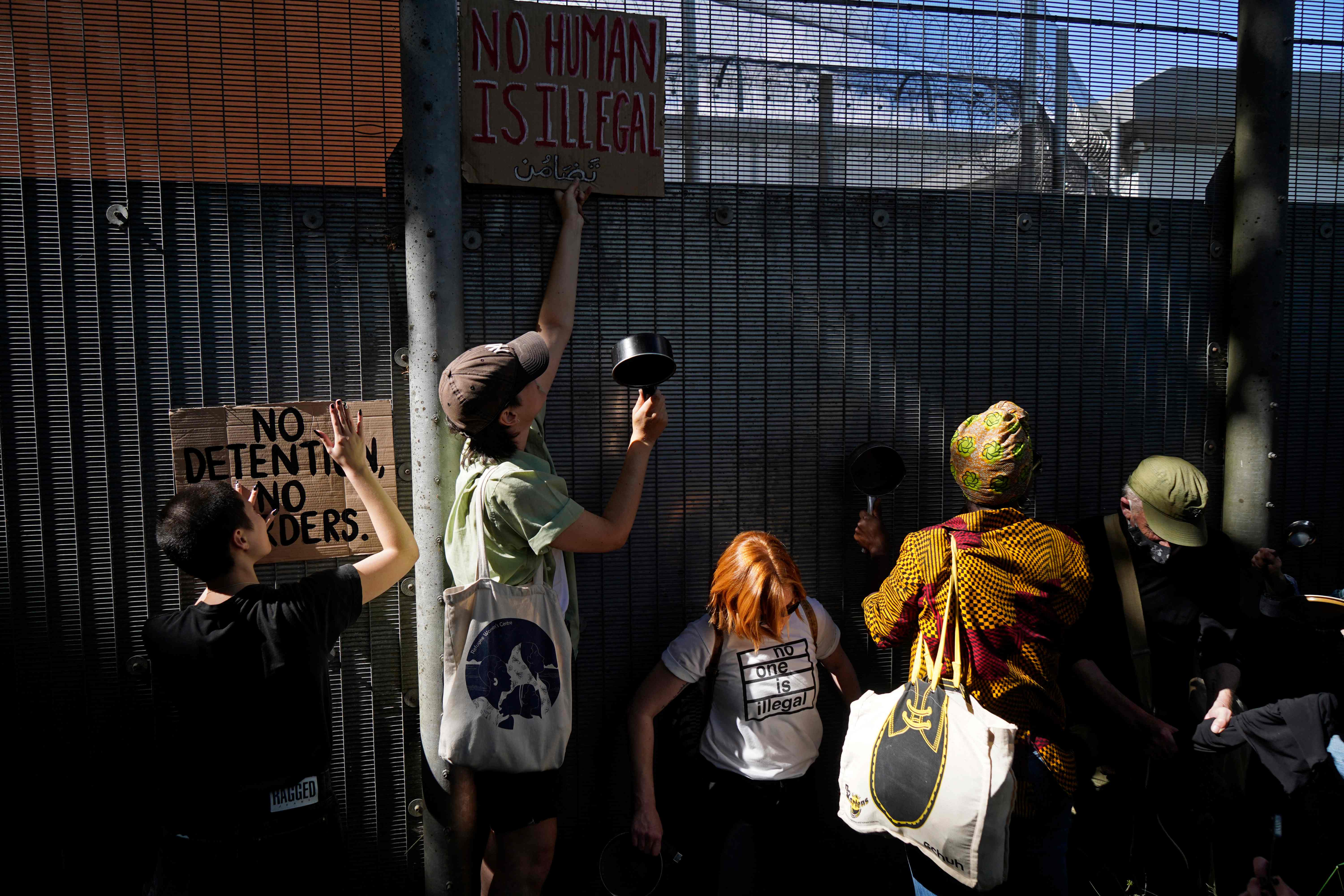 Protesters communicate with those inside at the perimeter fence of Brook House