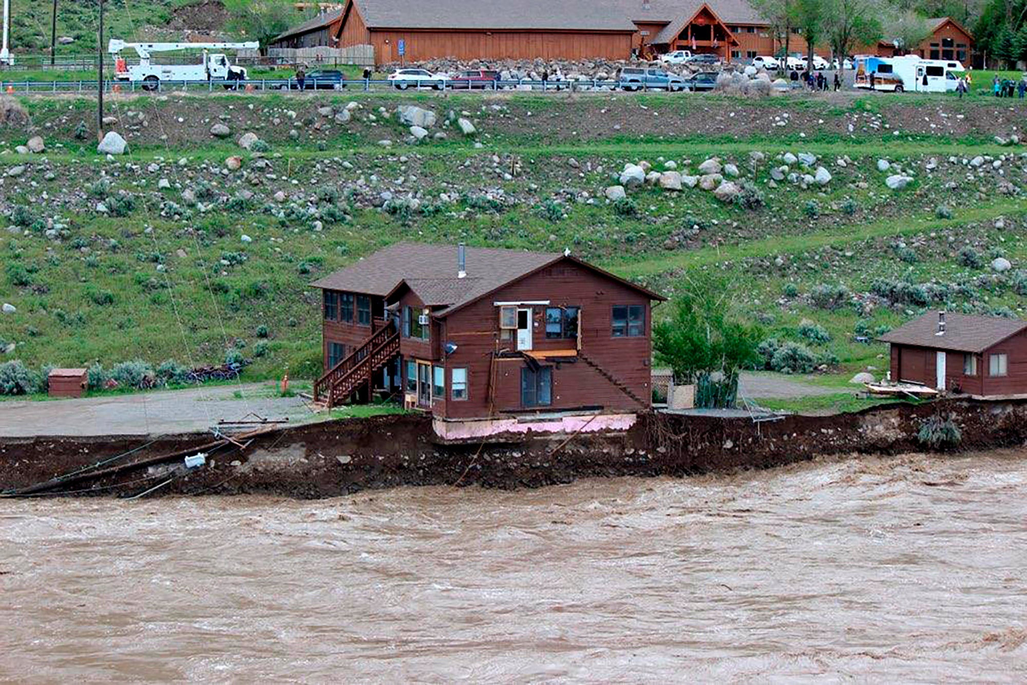 In this image provided by Sam Glotzbach, the flooding Yellowstone River undercuts the river bank, threatening a house and a garage in Gardiner, Mont., on June 13, 2022