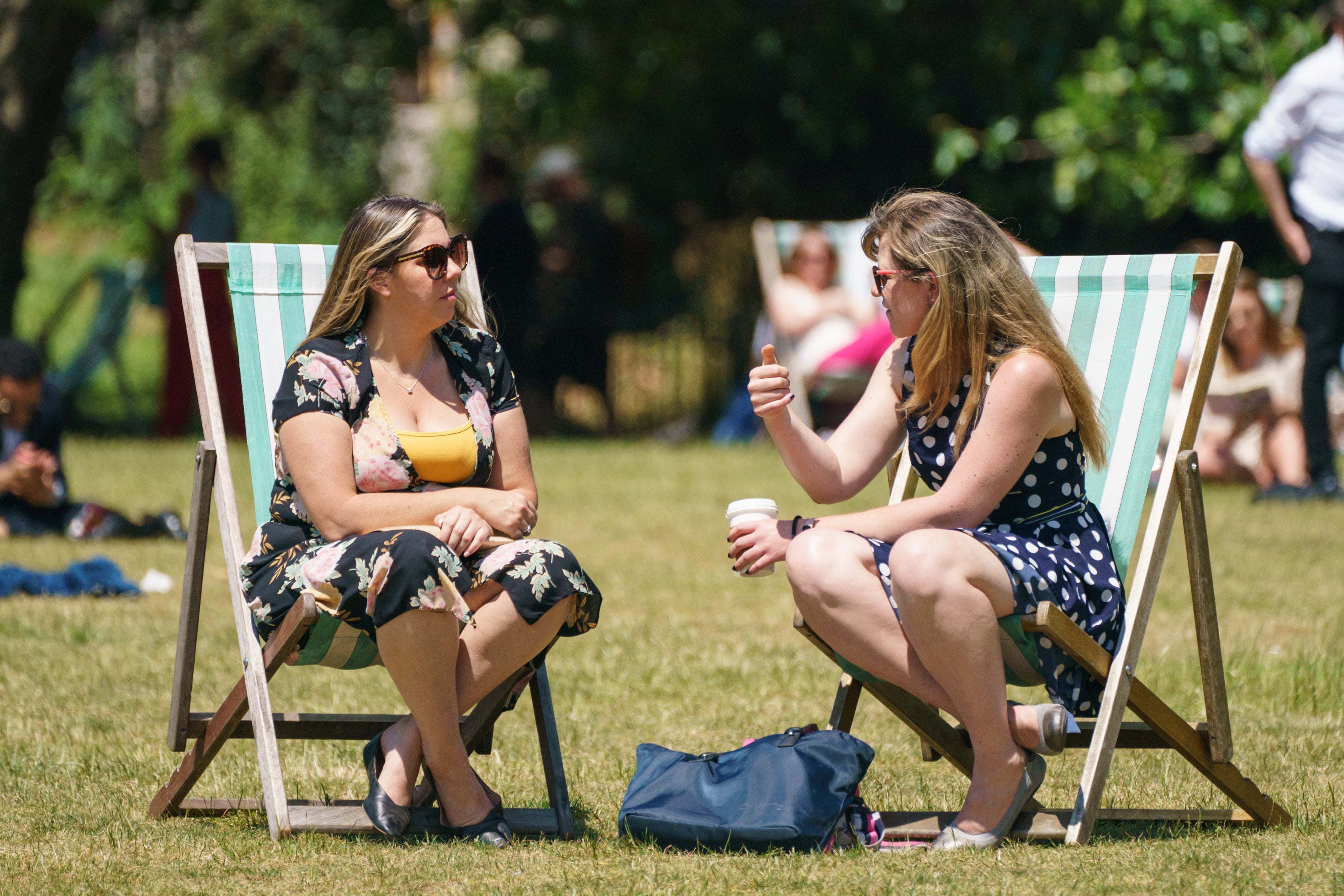 Two women sit in deck chairs as people enjoy the warm weather in Green Park, London (PA)